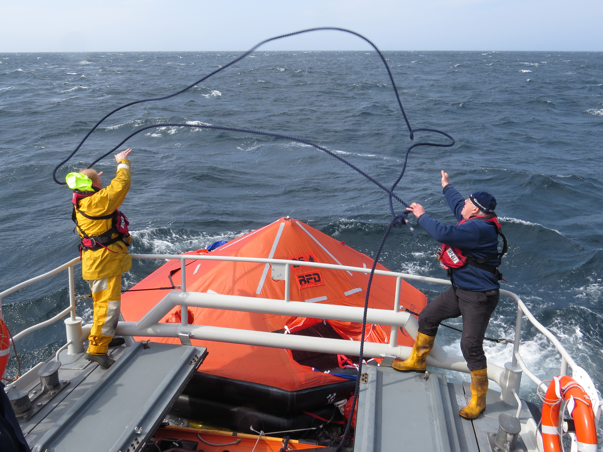 Two crew members lasso liferaft to secure to lifeboat