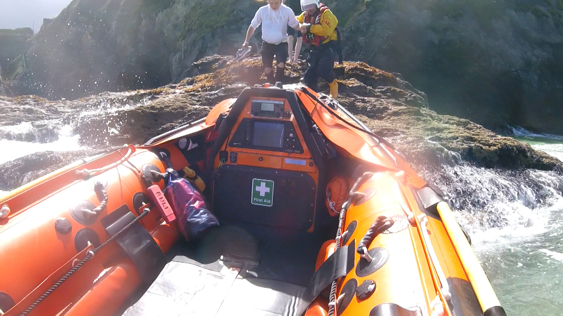 RNLI volunteer helps two people off rocks, onto lifeboat.