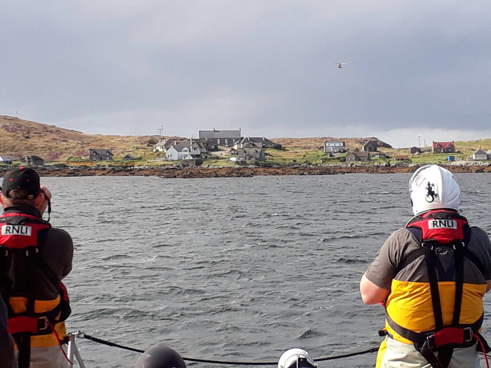 2 crew members standing on the boat looking towards the shore, one with the aid of binoculars.