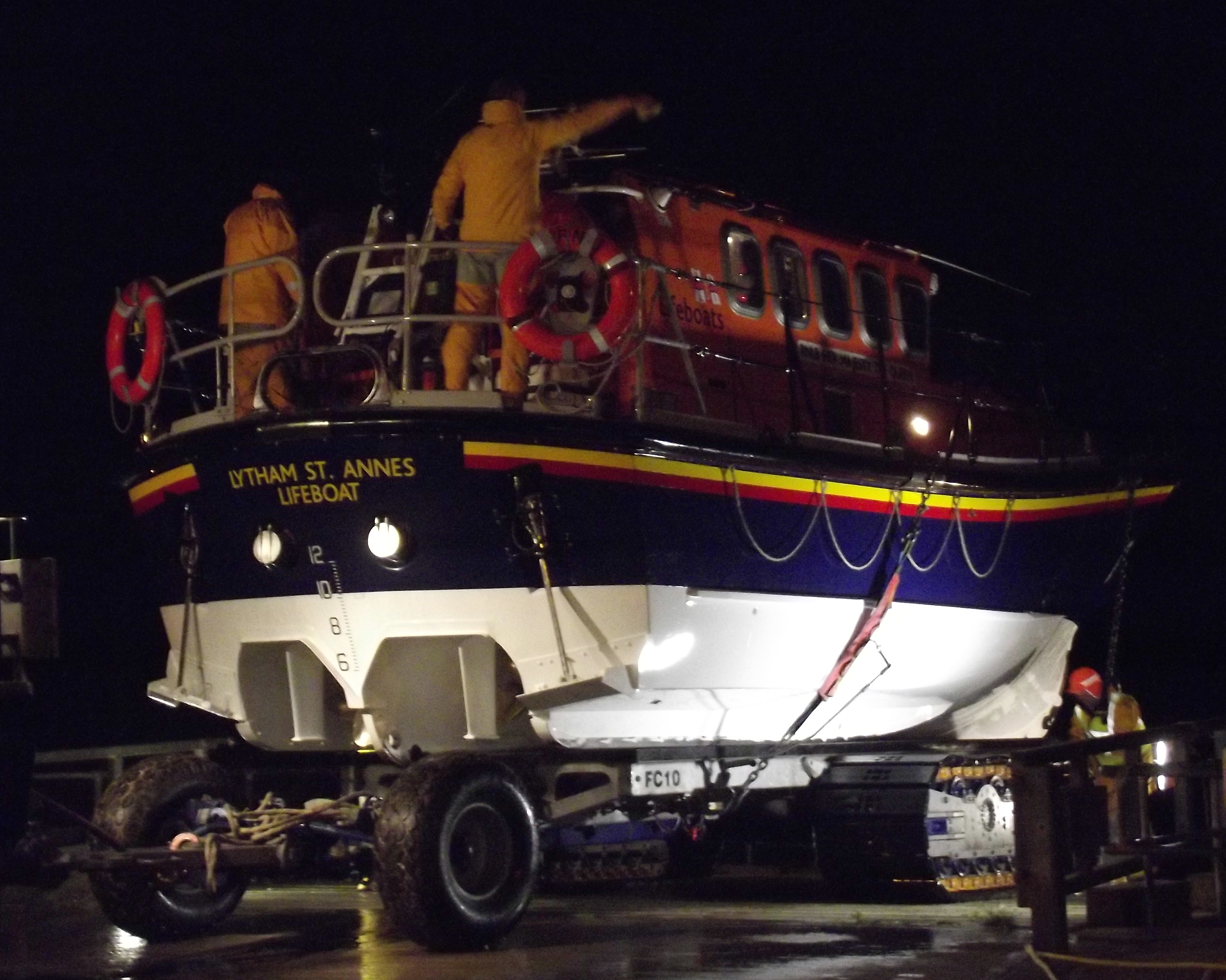 A lifeboat is on her carriage in the dark with crew members cleaning and checking her over.