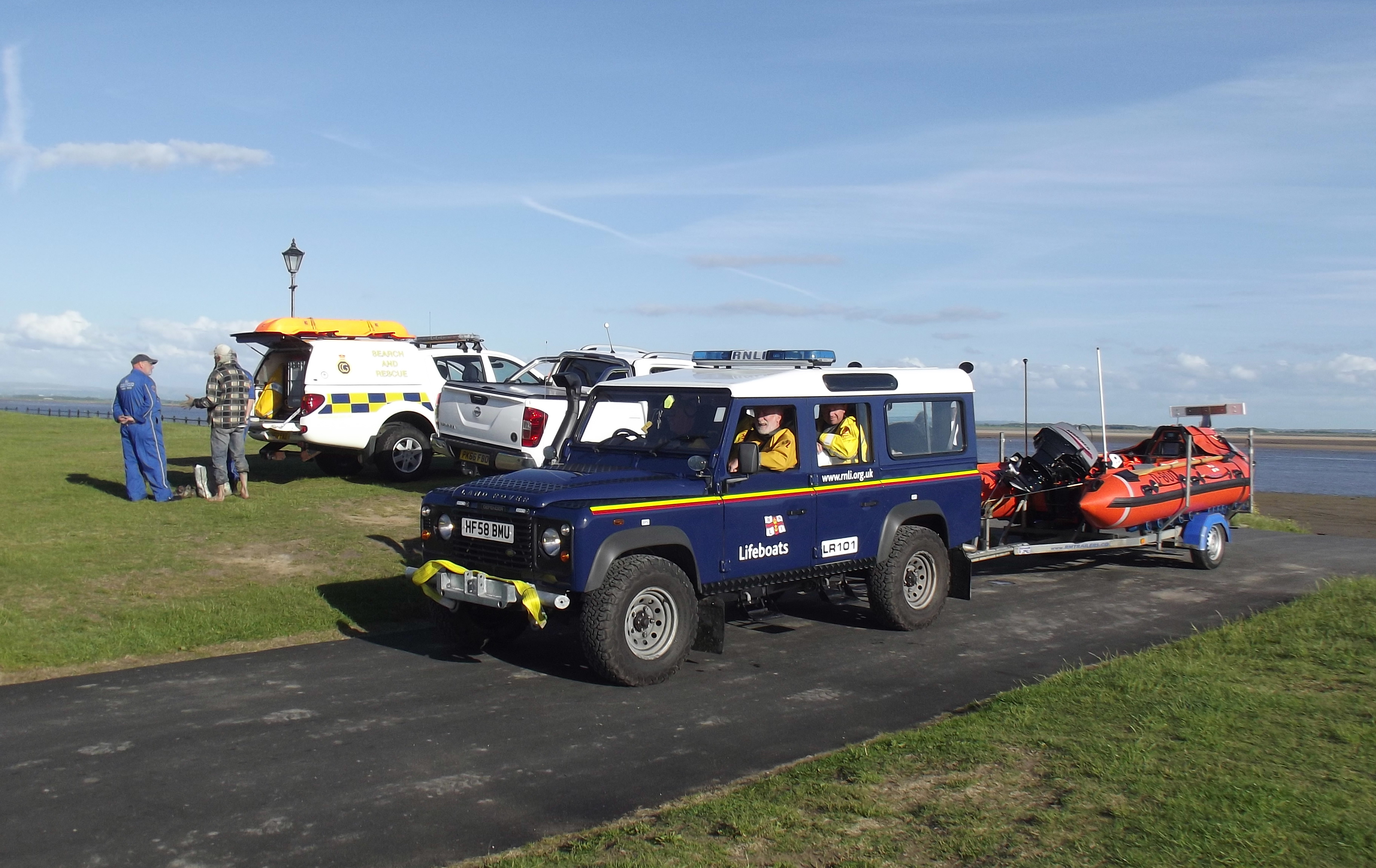 A lifeboat Land Rover tows the Lytham St Annes ILB past two Coastguard vehicles and Coastguards ensuring the rescued man is unharmed