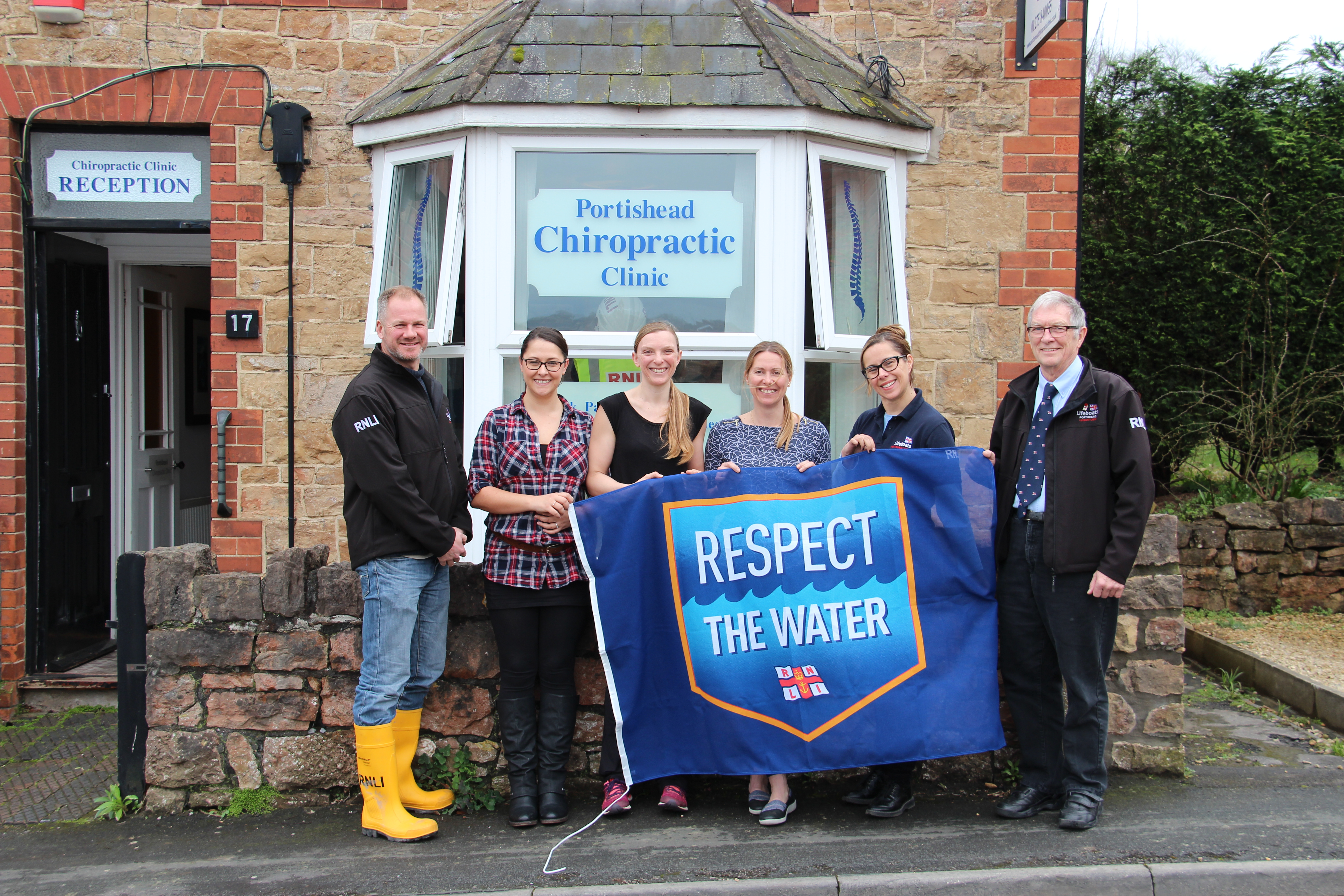 Staff and volunteer crew stand outside the Portishead Chiropractic Clinic with RNLI Respect the Water flag