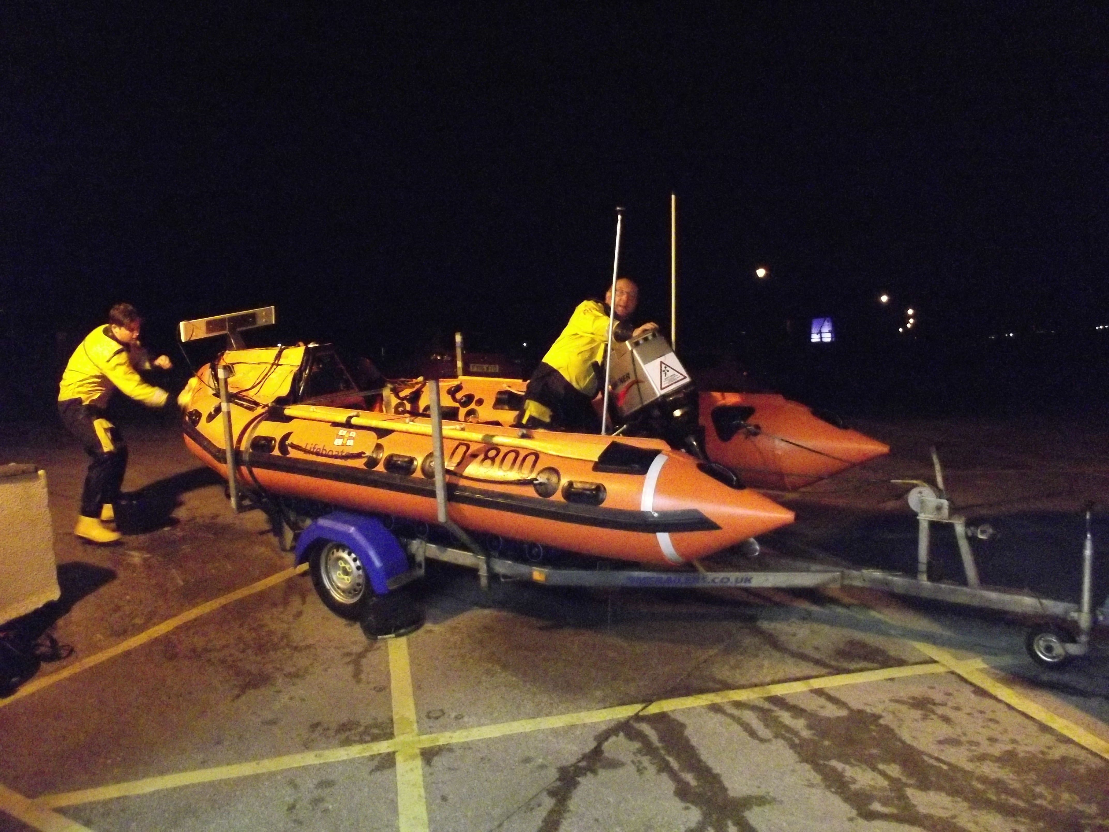 An inshore lifeboat is being washed off by two crew members at night 
