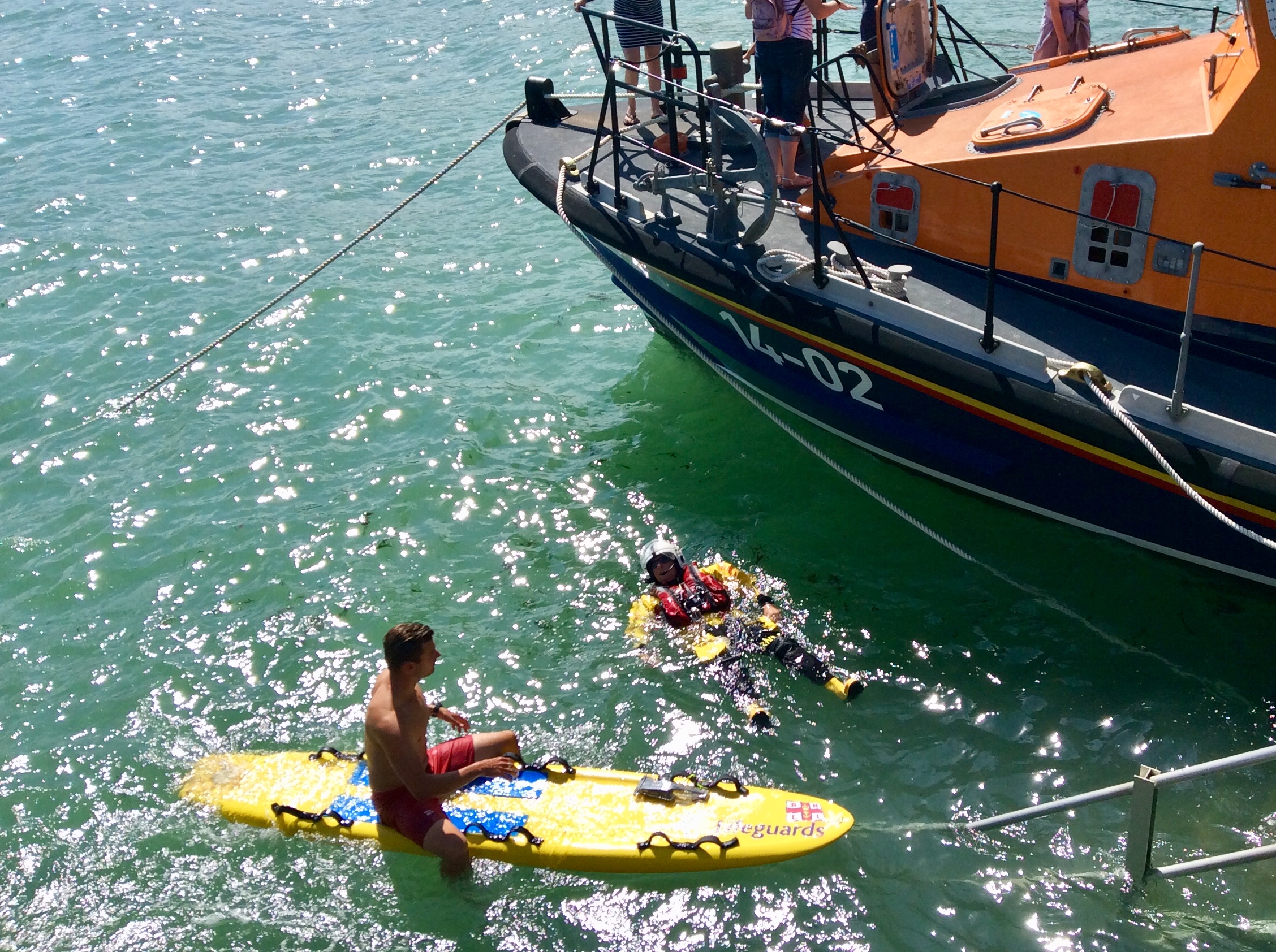 RNLI Beach lifeguard on his paddle board and RNLI crew member demonstrating the 'Float to Live' message with the 'Esme Anderson' lifeboat next to them.