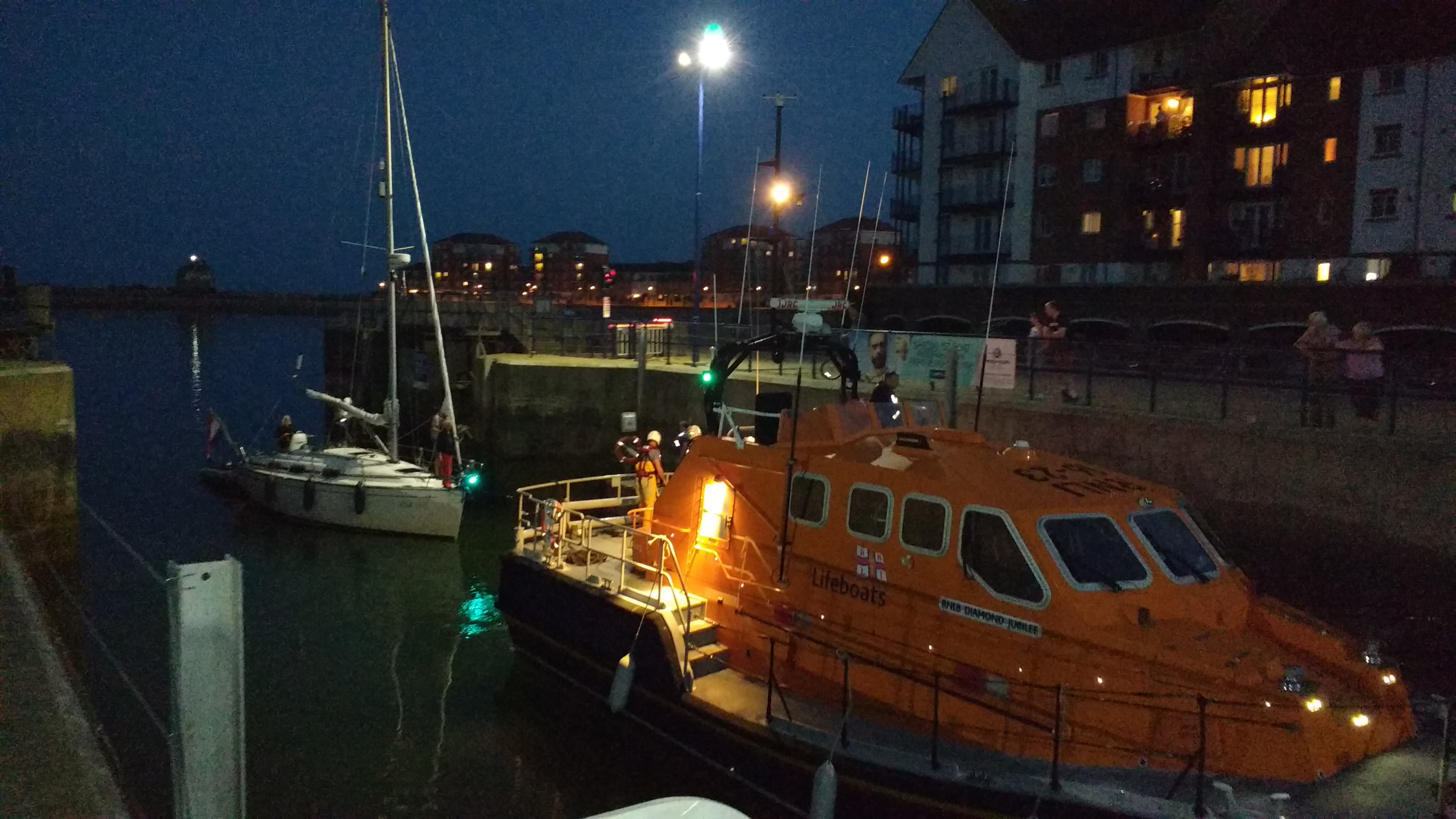 Shot of the yacht at night being towed into harbour by the lifeboat.