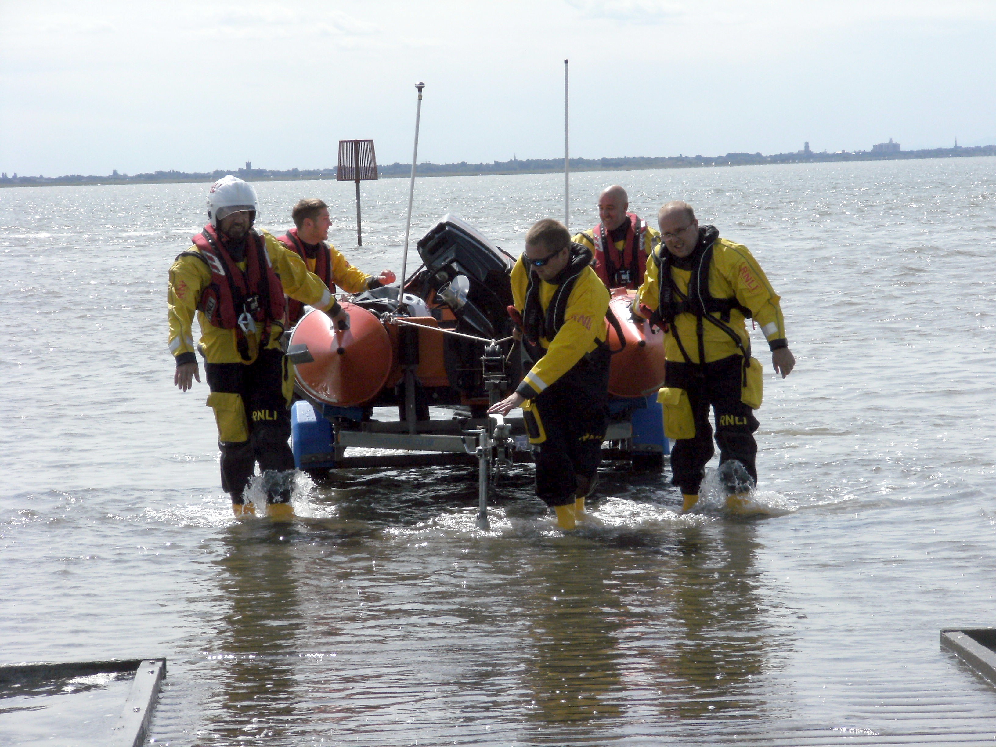 A group of crew members pull an inshore lifeboat through the water after recovering her onto her carriage.