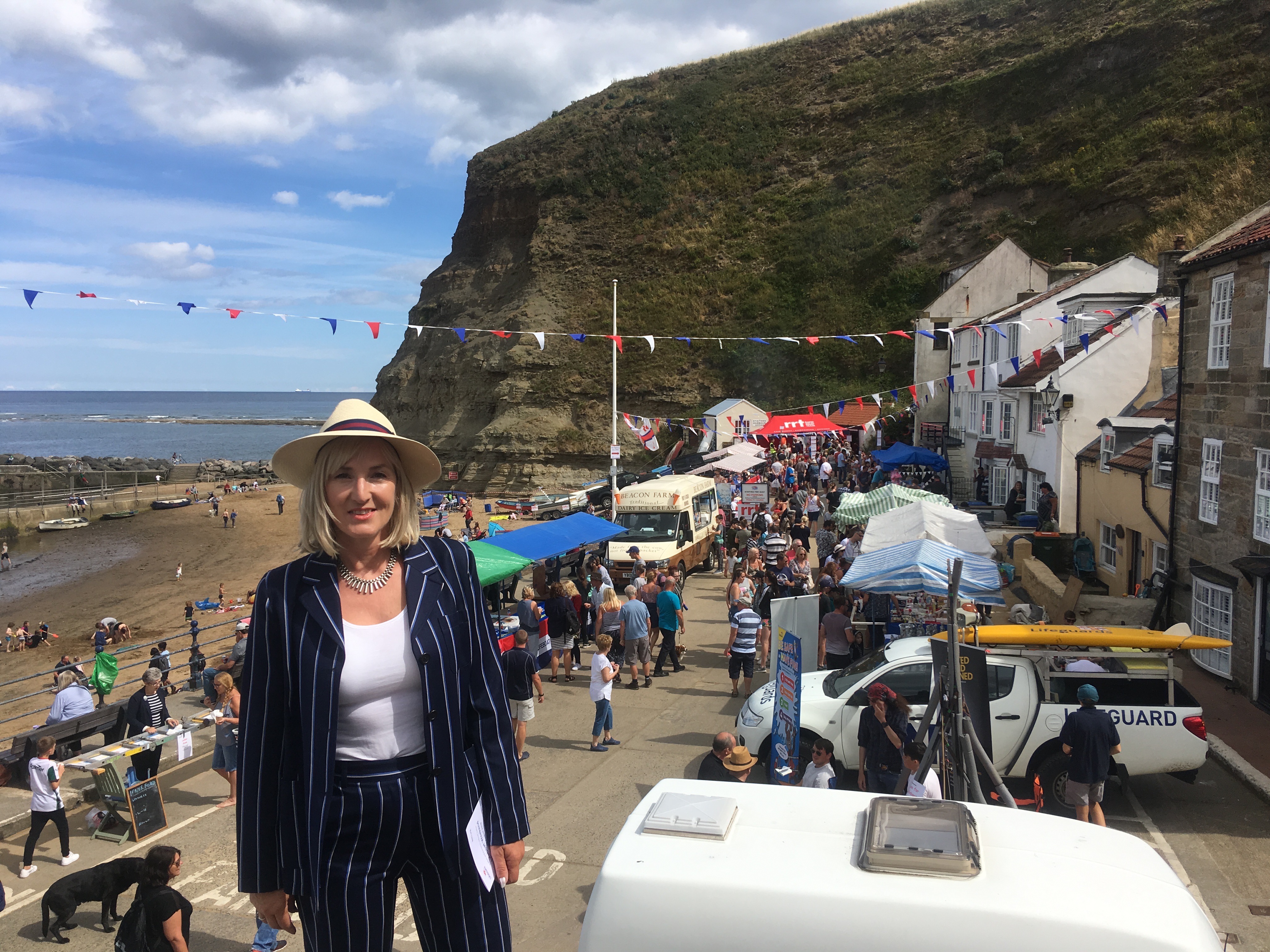 Woman TV presenter above row of stalls at Staithes harbour front