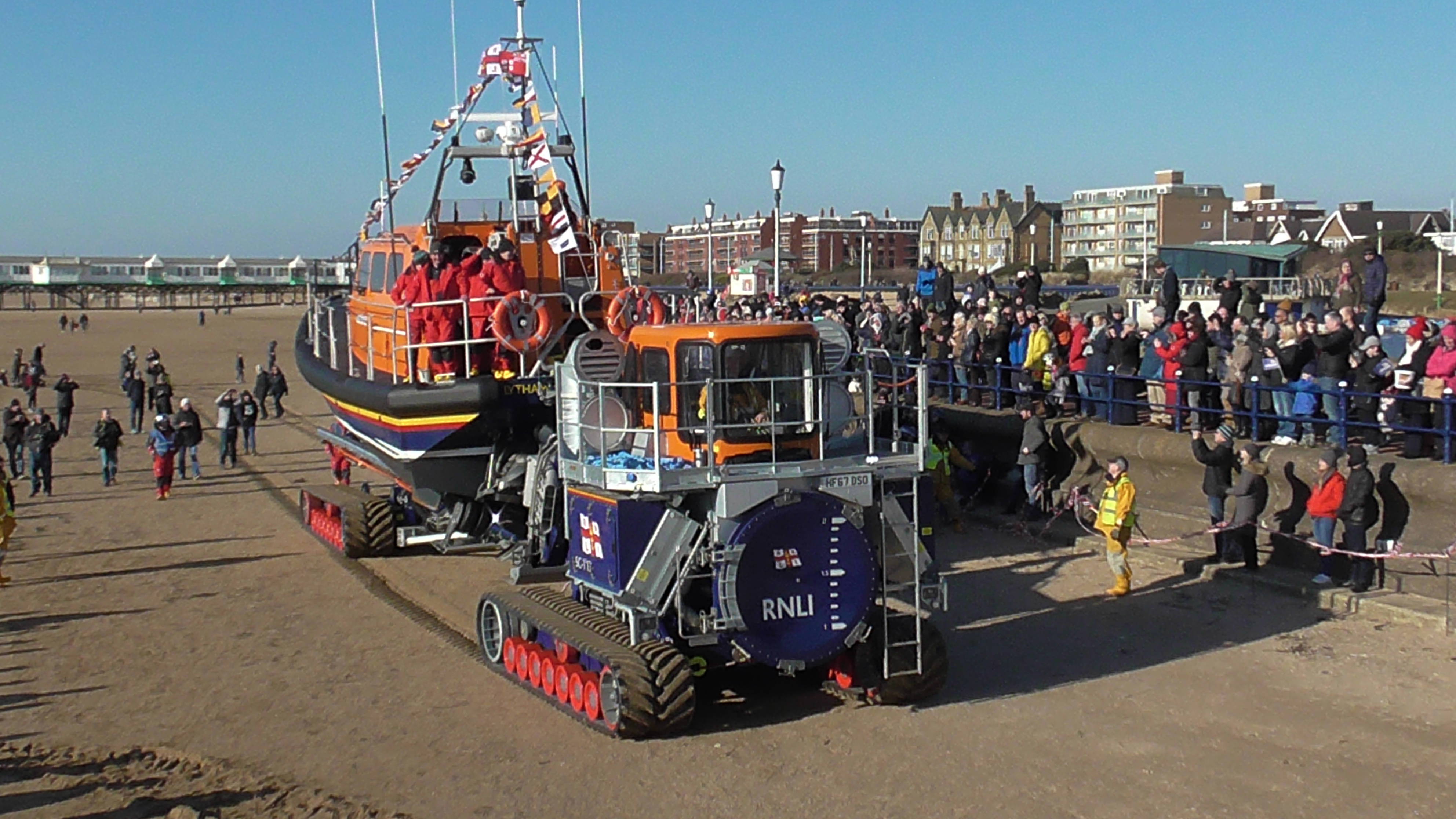 a lifeboat surrounded by people sits on her launching tractor and carriage