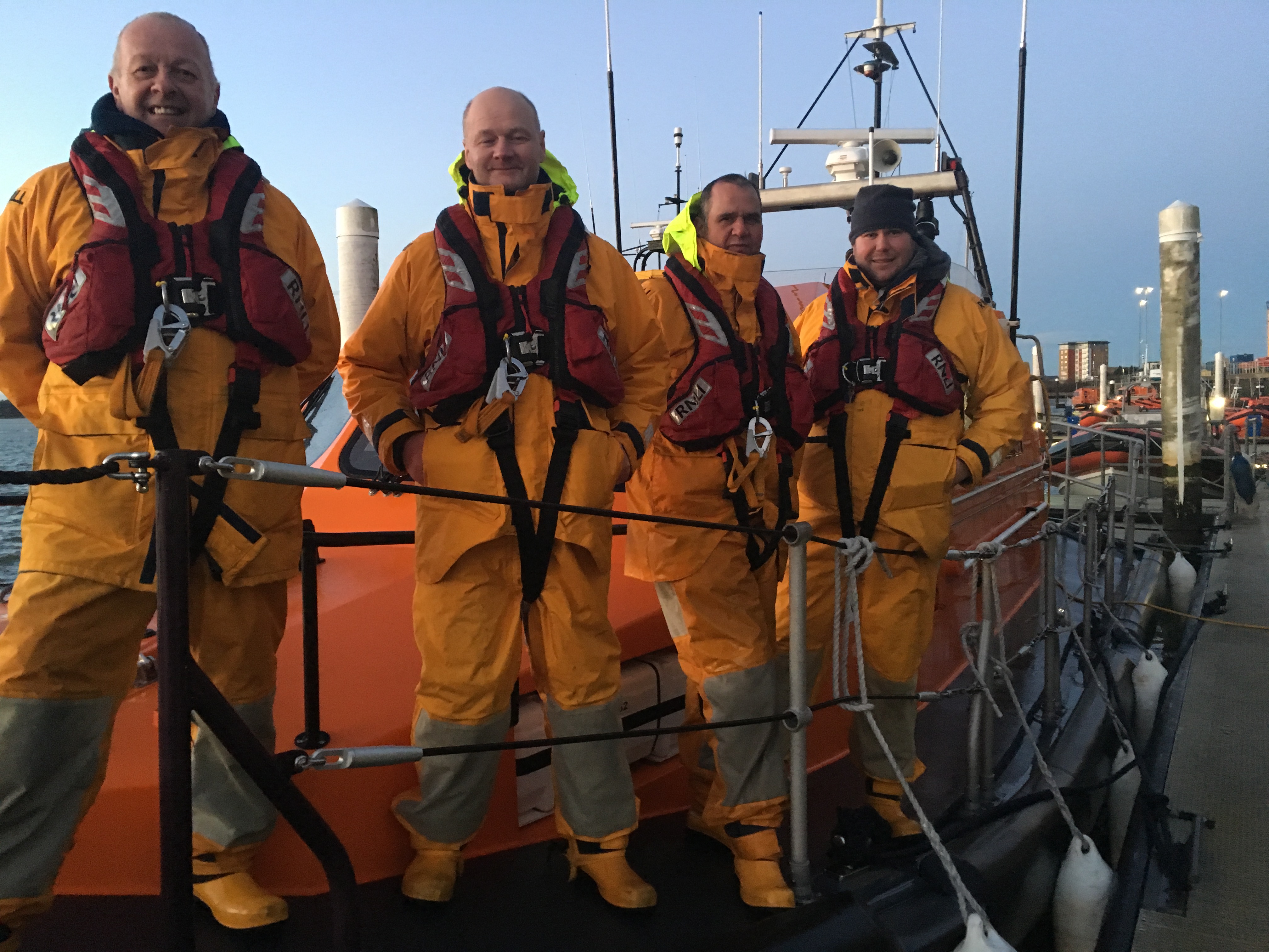 Four crew members in protective clothing stand on the deck of a lifeboat