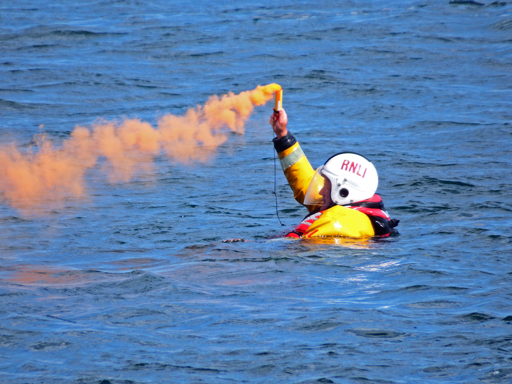 Crew member in sea holding smoking flare in man overboard exercise