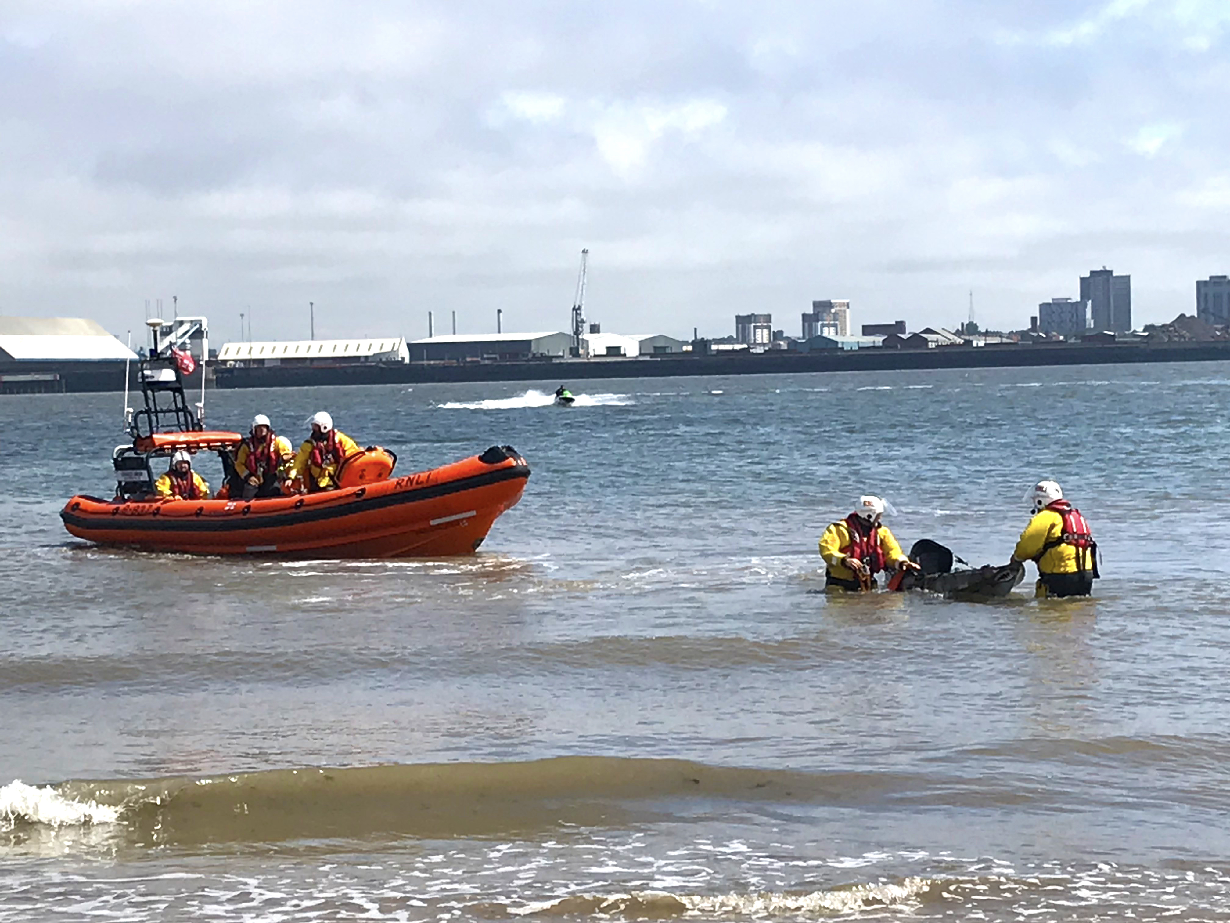 Two RNLI crew members bring a kayak to shore while the inshore lifeboat floats nearby