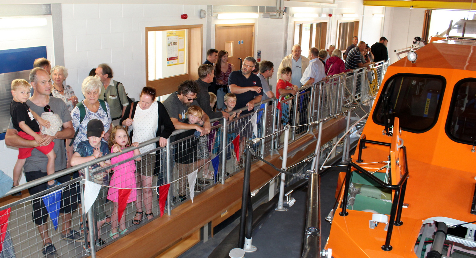 Members of the public look at an orange RNLI lifeboat from a balcony.