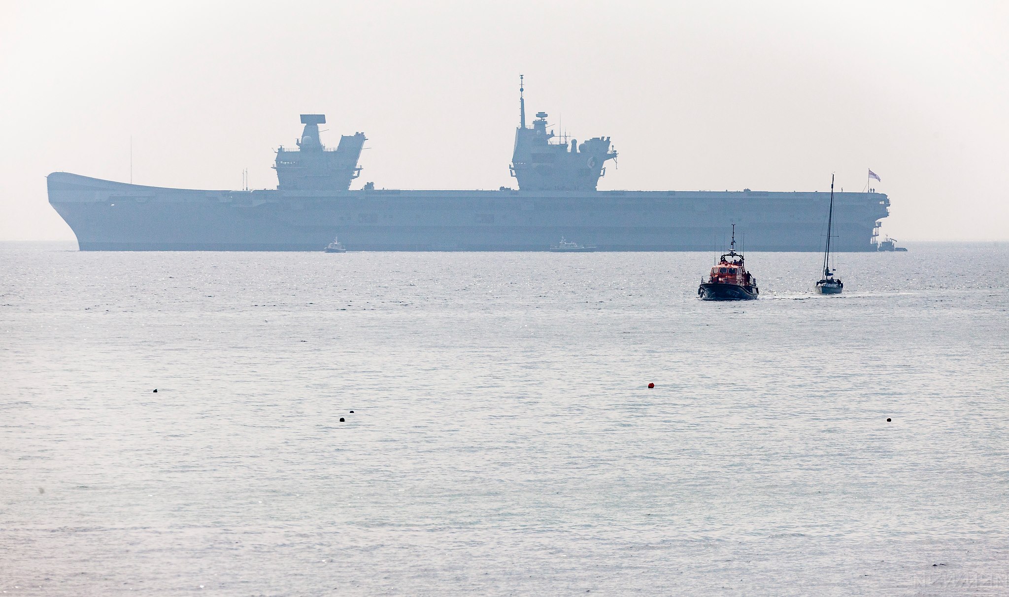 The Lizard RNLI Lifeboat towing the yacht "Fair Emma" accompanied by a huge vessel in the distance.
