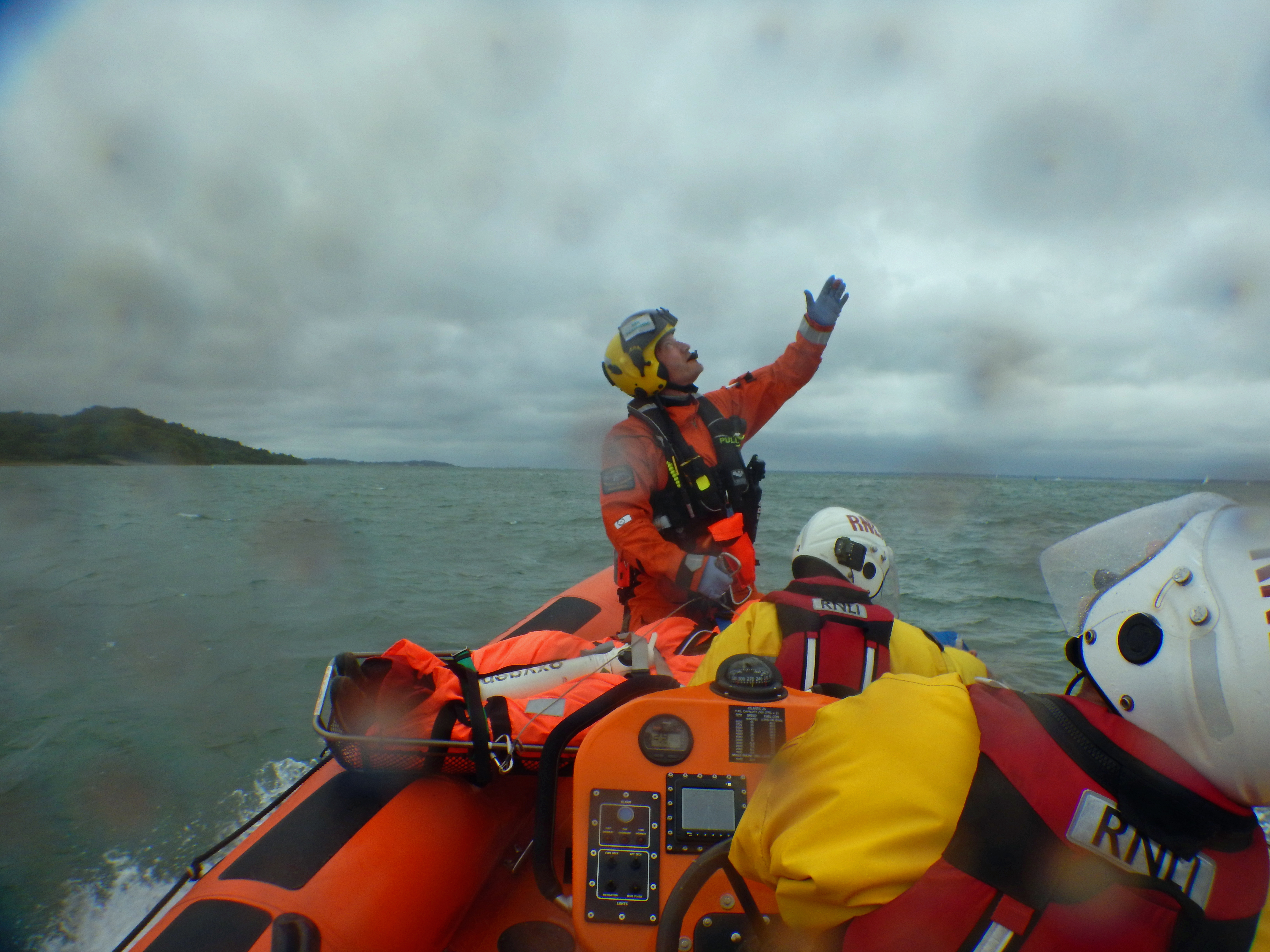 Paramedic, aboard the lifeboat with the collapsed man, signals to the hovering helicopter.
