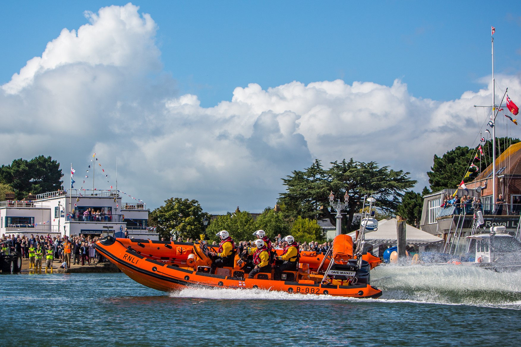 Lymington RNLI Lifeboat at speed in foreground, Blue sky with fluffy clouds background