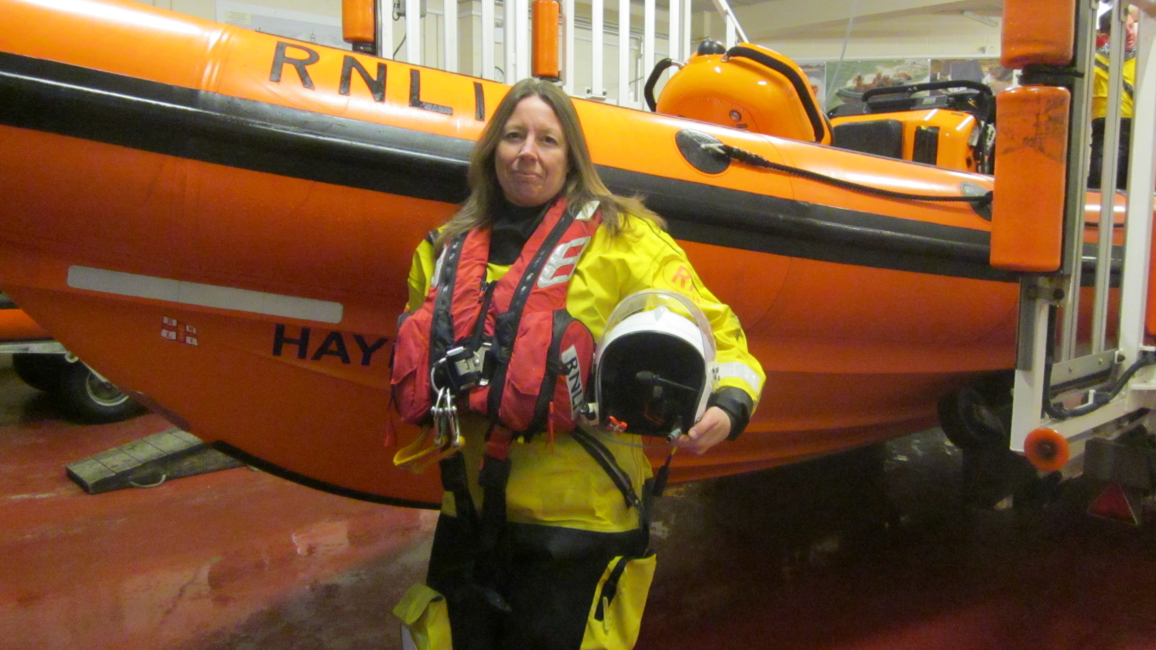 A photo of crew member Sharon Swan in her PPE kit in front of the inshore lifeboat used in the rescue.