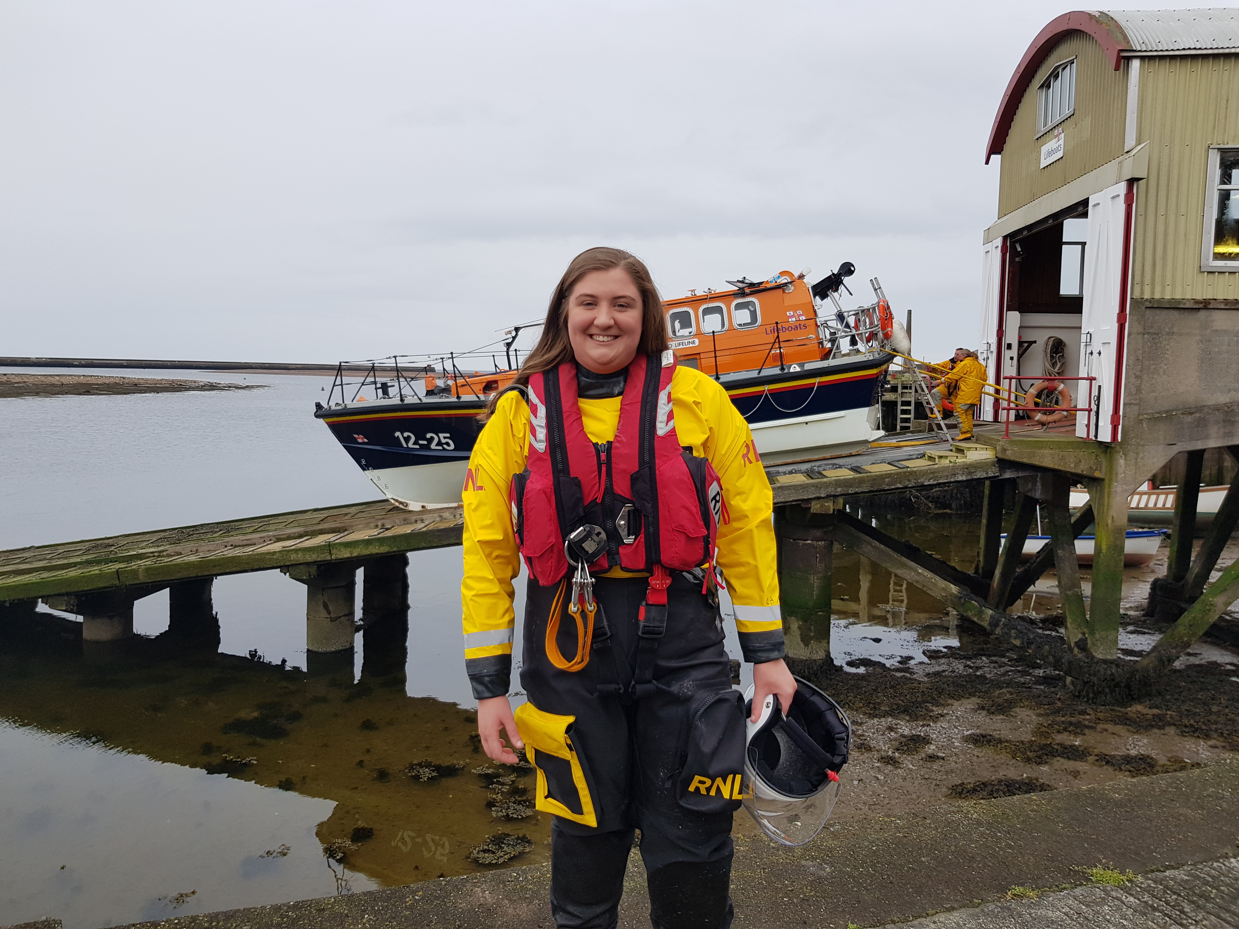 Christi Avril in her RNLI Inshore Lifeboat kit with Berwick-upon-Tweed all-weather lifeboat behind