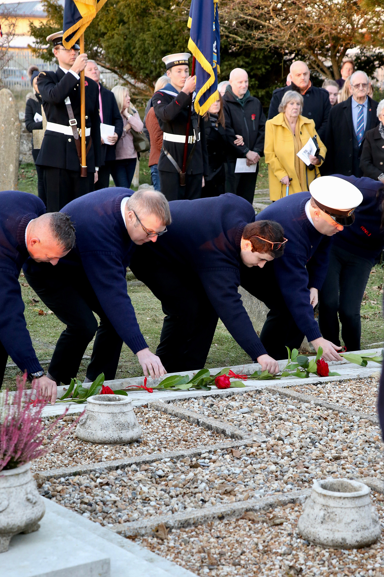 Four RNLI volunteers bend down to place a red rose on the names of four of the crew who were lost in the Mary Stanford disaster