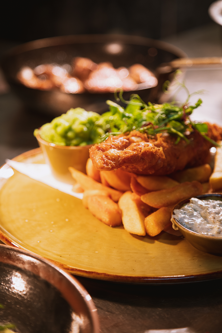 Fish placed on top of a pile of chips with some mushy peas and tartar sauce