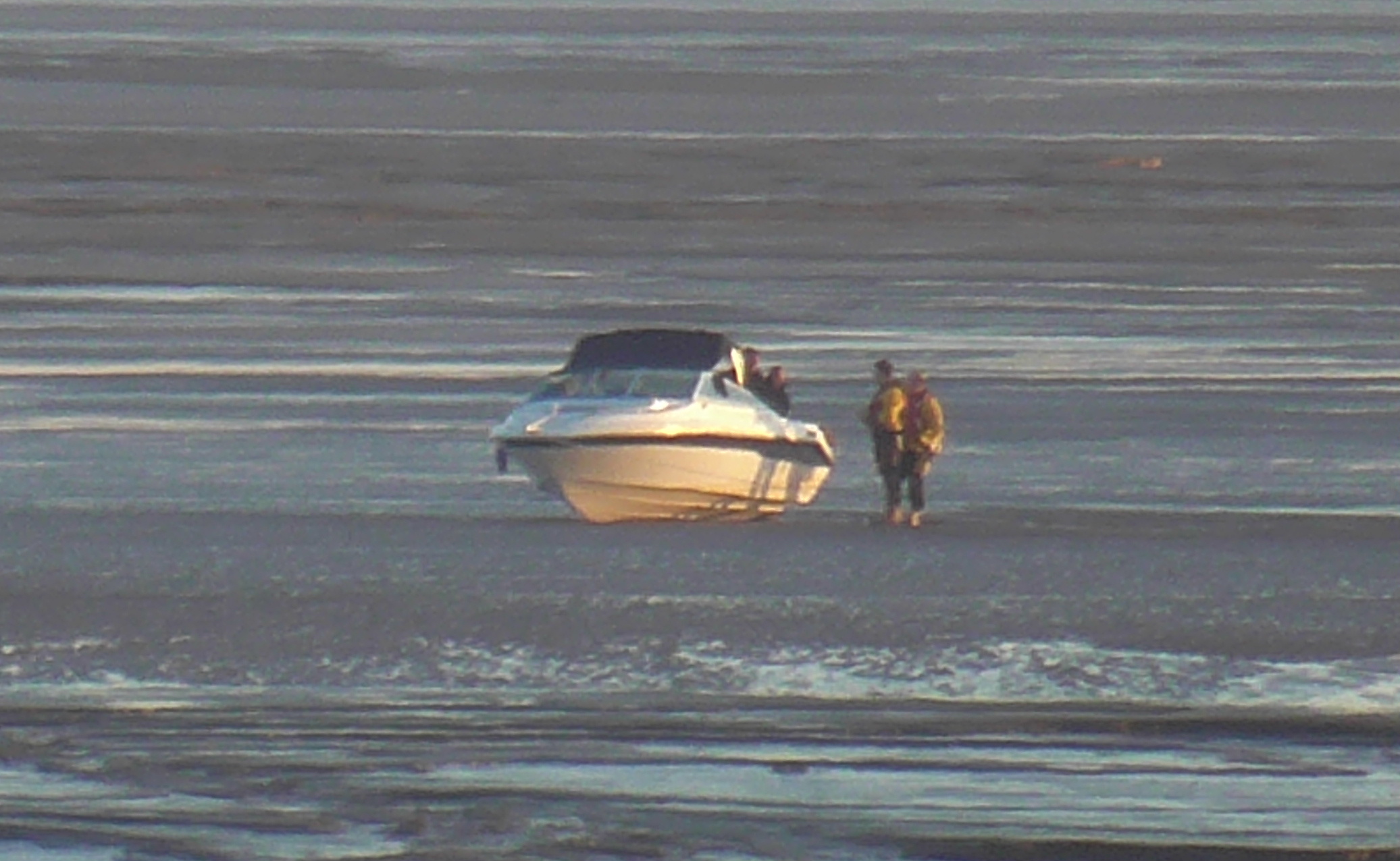 A motor boat sits aground with two lifeboat crew standing alongside