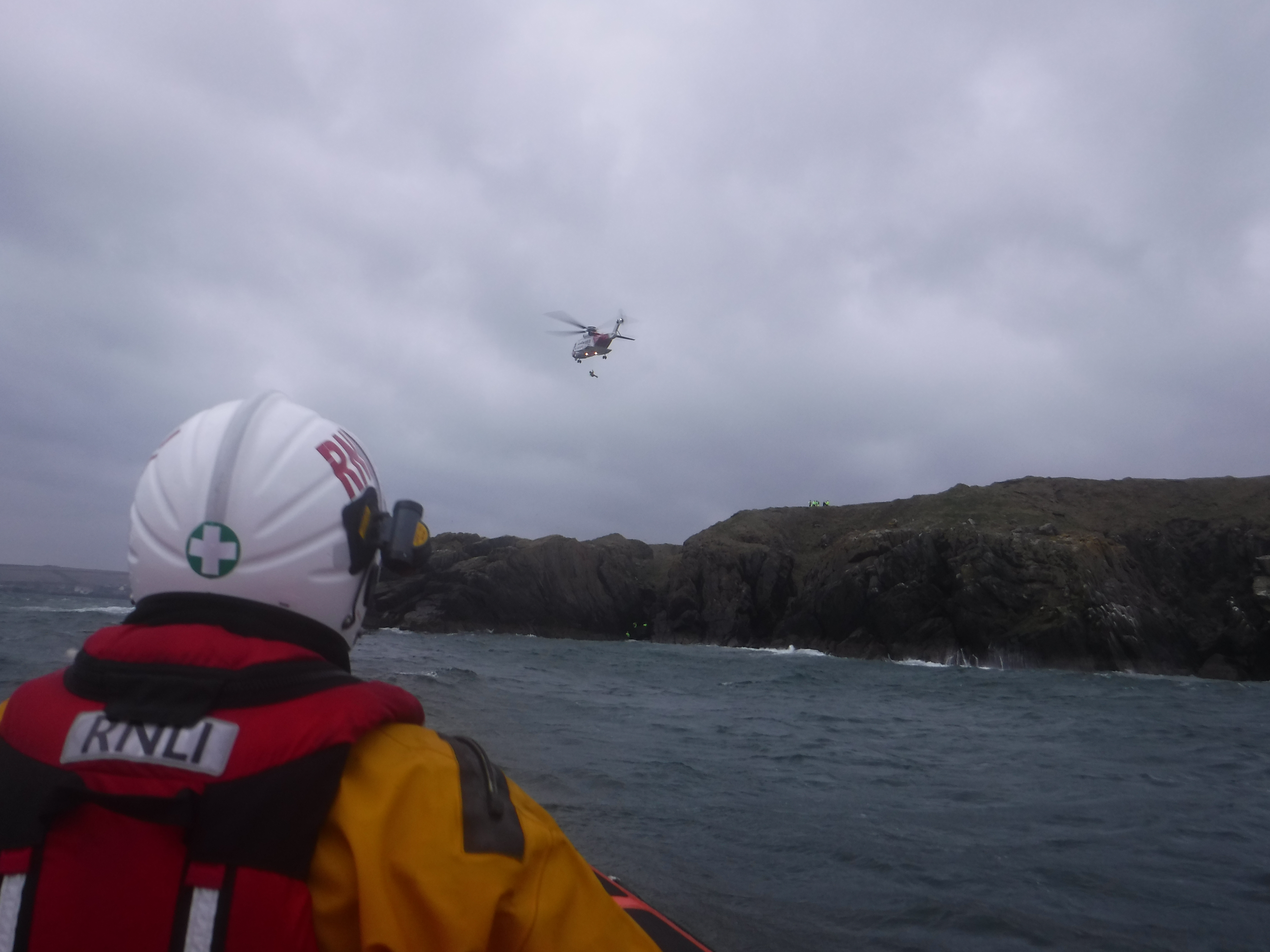Coastguard helicopter Rescue 951 winching the casualty to safety with RNLI crew member in the foreground