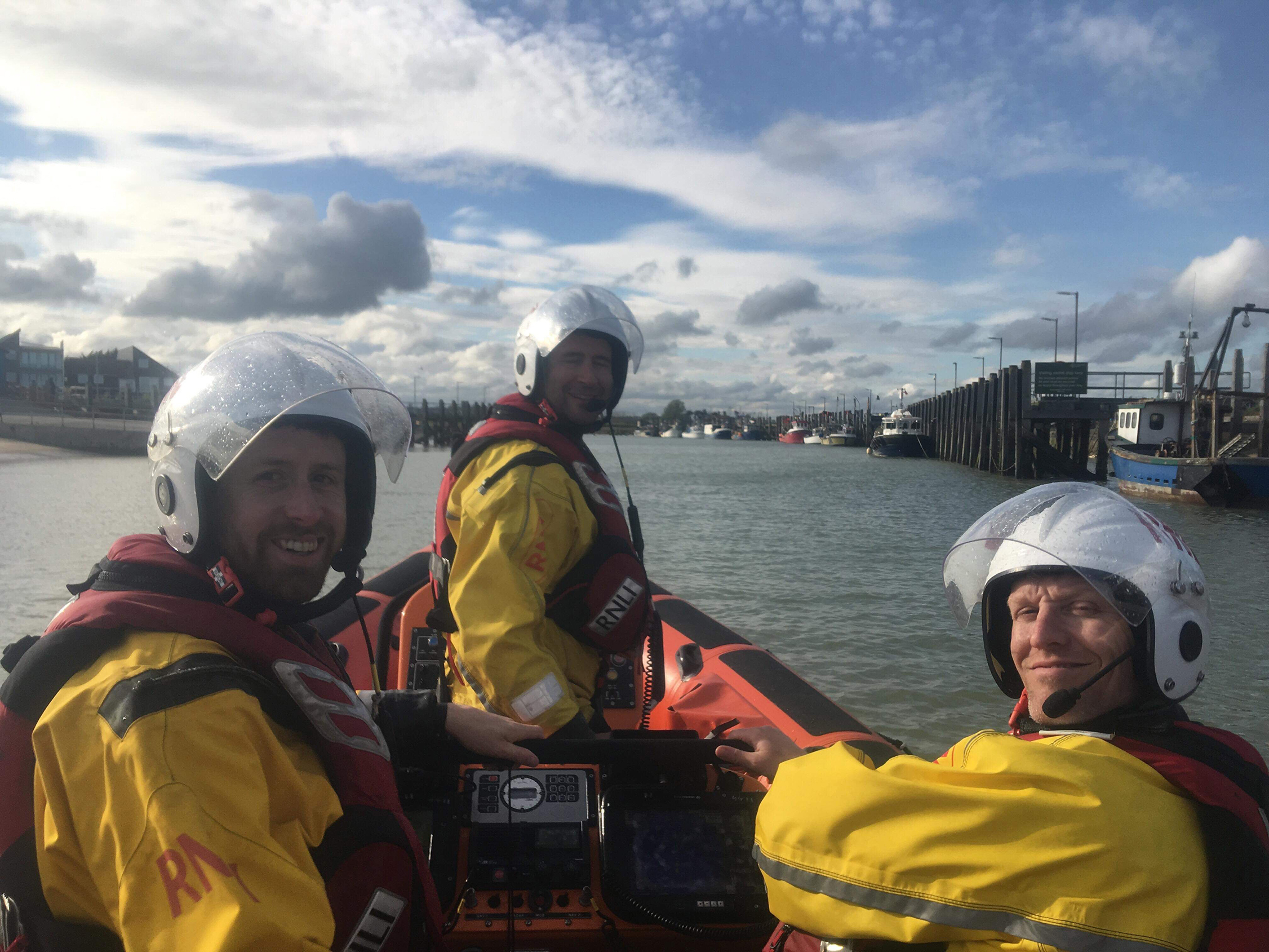 Tim and and two crew members turn back towards the camera as the lifeboat proceeds down-river
