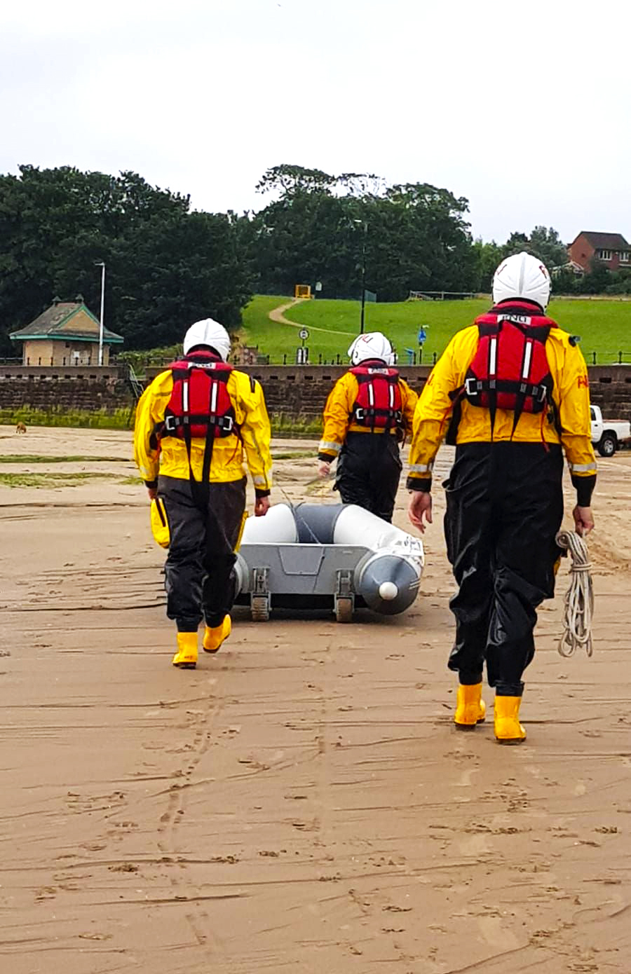 The backs of three RNLI shore crew as they pull the dinghy up the sand 