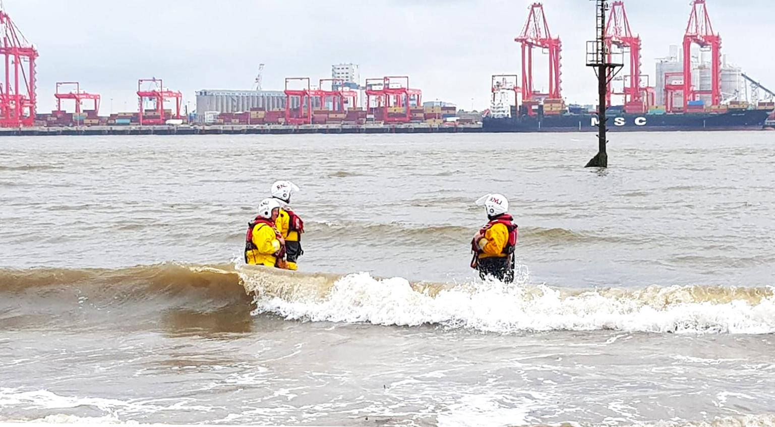 Three shore crew around thigh deep in water as they await the lifeboat