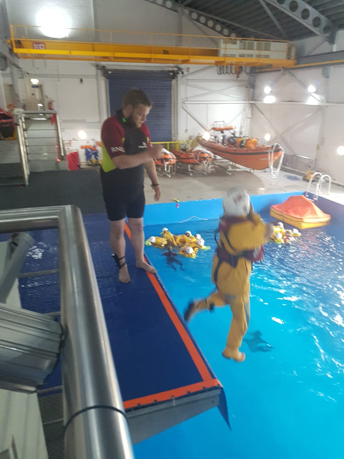 A volunteer cre-member jumps into the water of the training tank from a high platform as part of the Sea Survival course