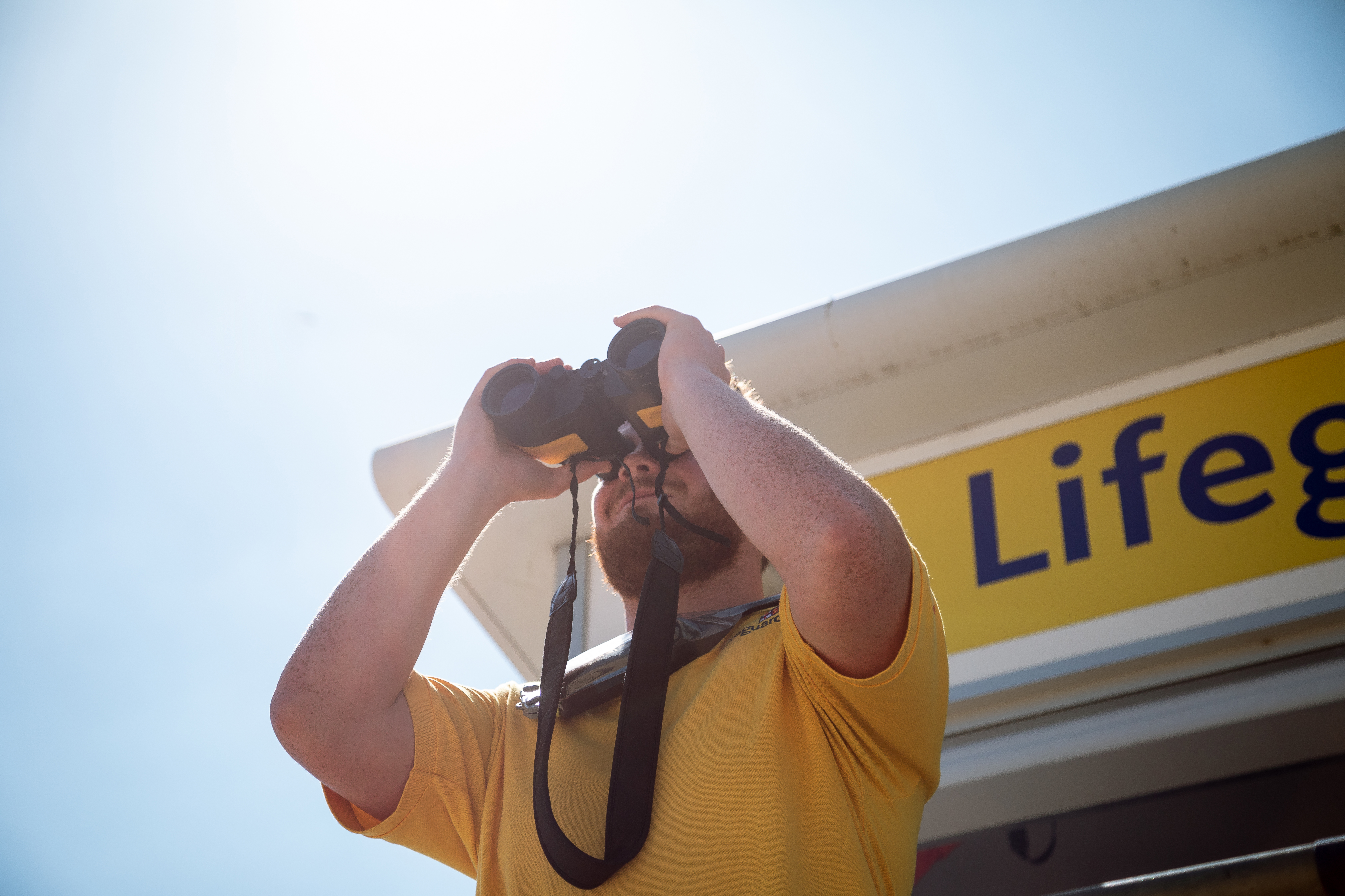 Lifeguard monitors the beach from lifeguard hut in using binoculars. 
