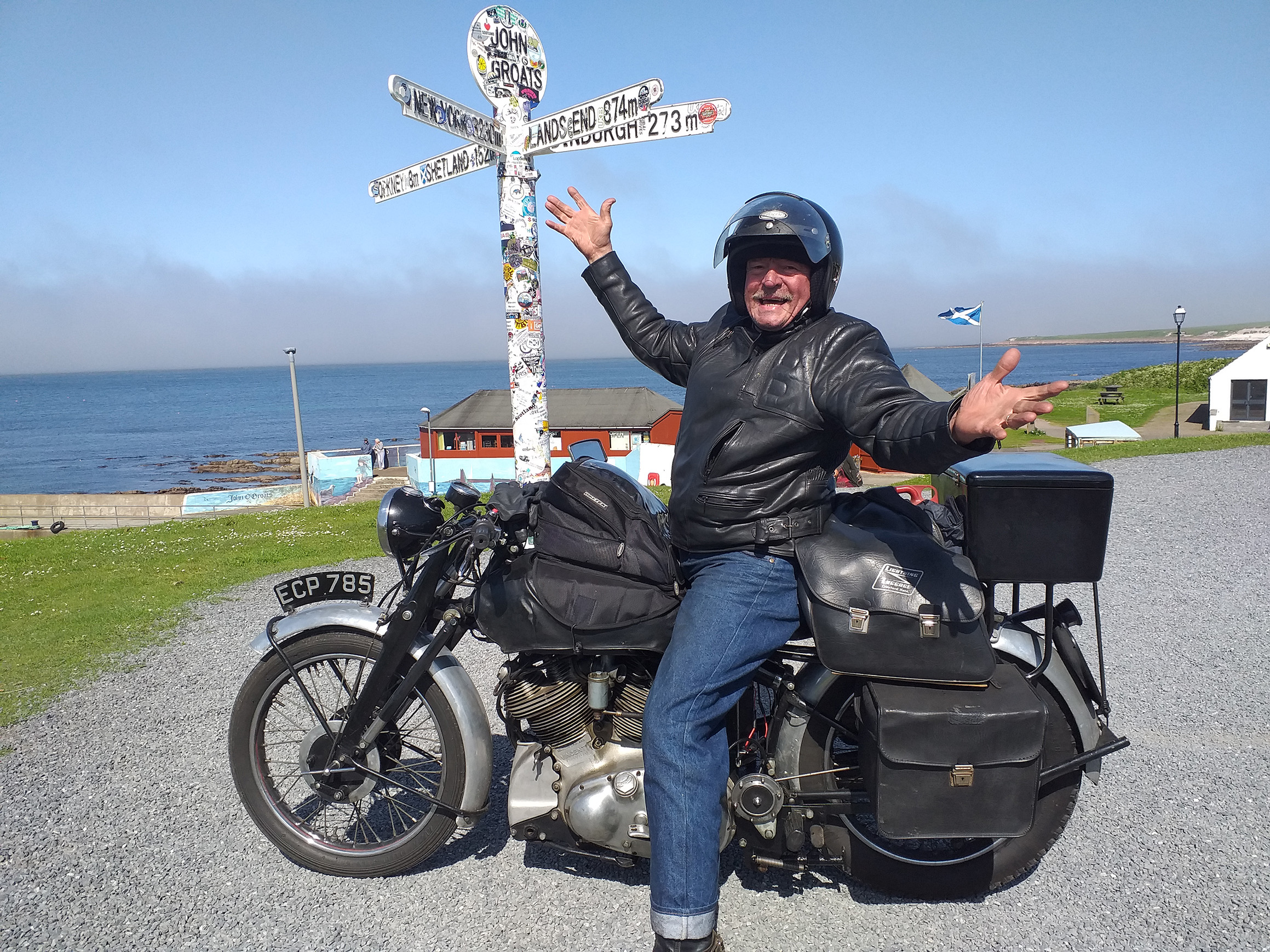 John sitting on his Vincent motorbike in front of the signpost at Land's end