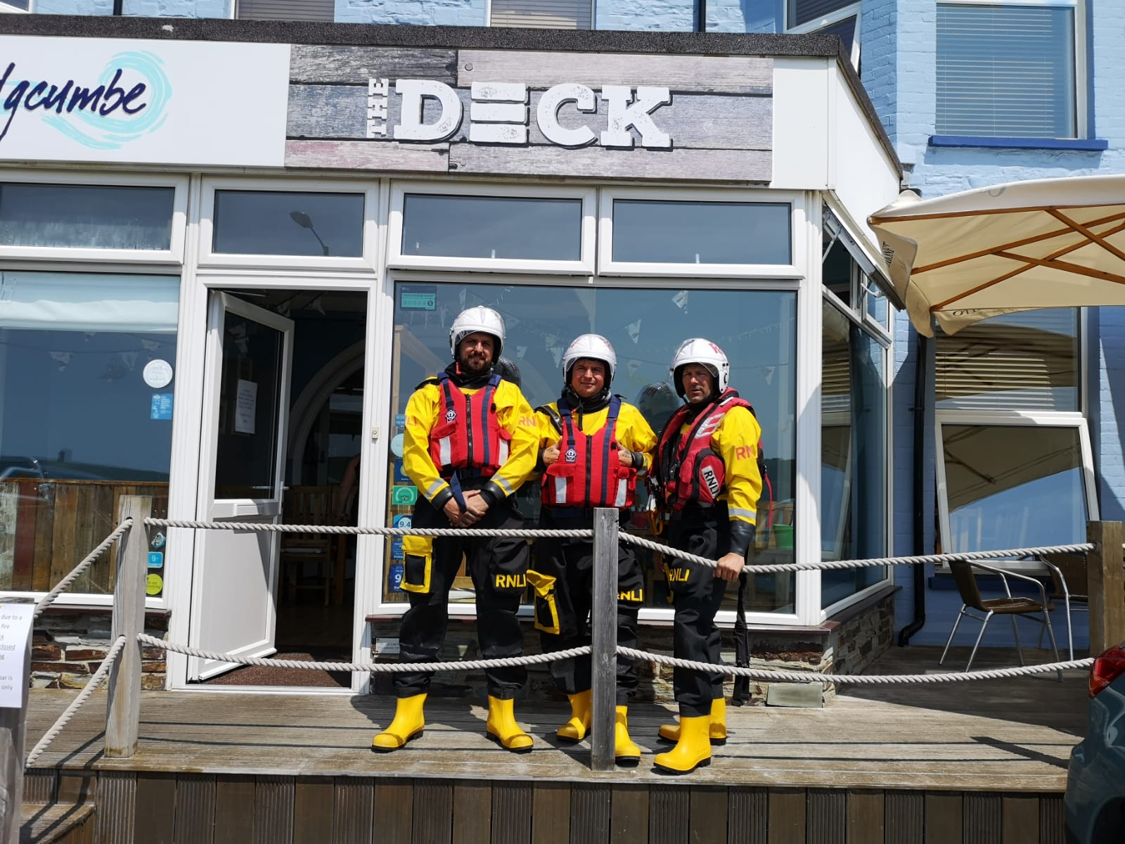 Three volunteer crew members in lifeboat kit outside the Deck bar and restaurant in Bude