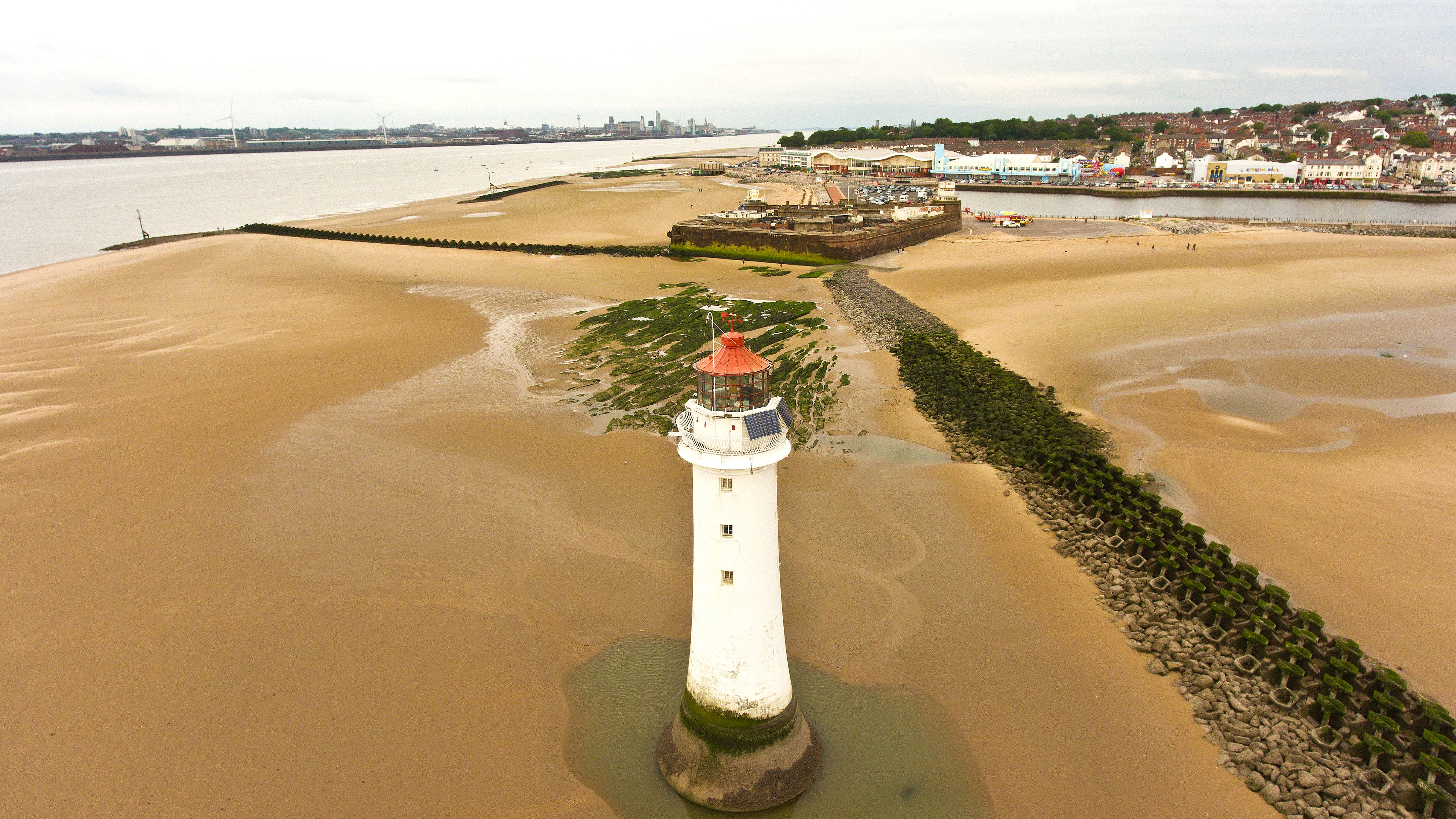 Lighthouse surrounded by sand with water, Fort Perch Rock and the multi-agency group in the background