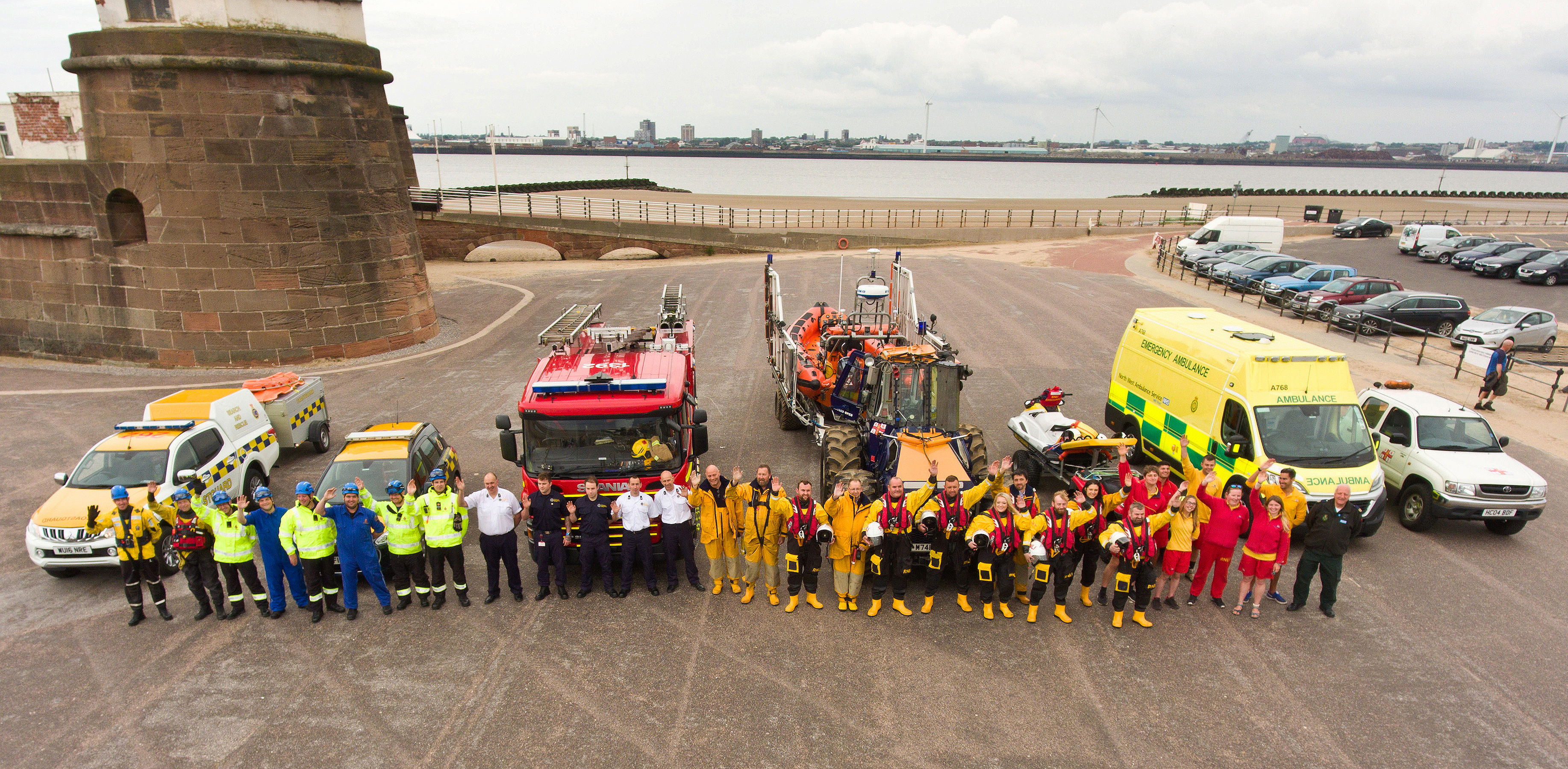 Line up of Wirral agences waving in front of their vehicles with Fort Perch Rock in the background