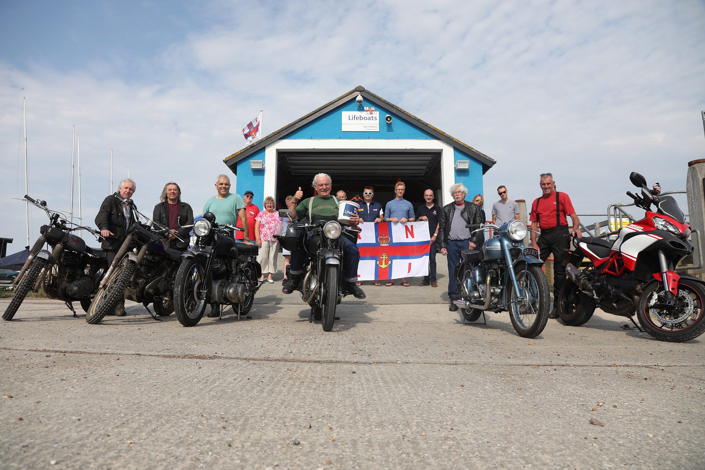 John Newson and friends with motor bikes in front of the boathouse with crew and villagers