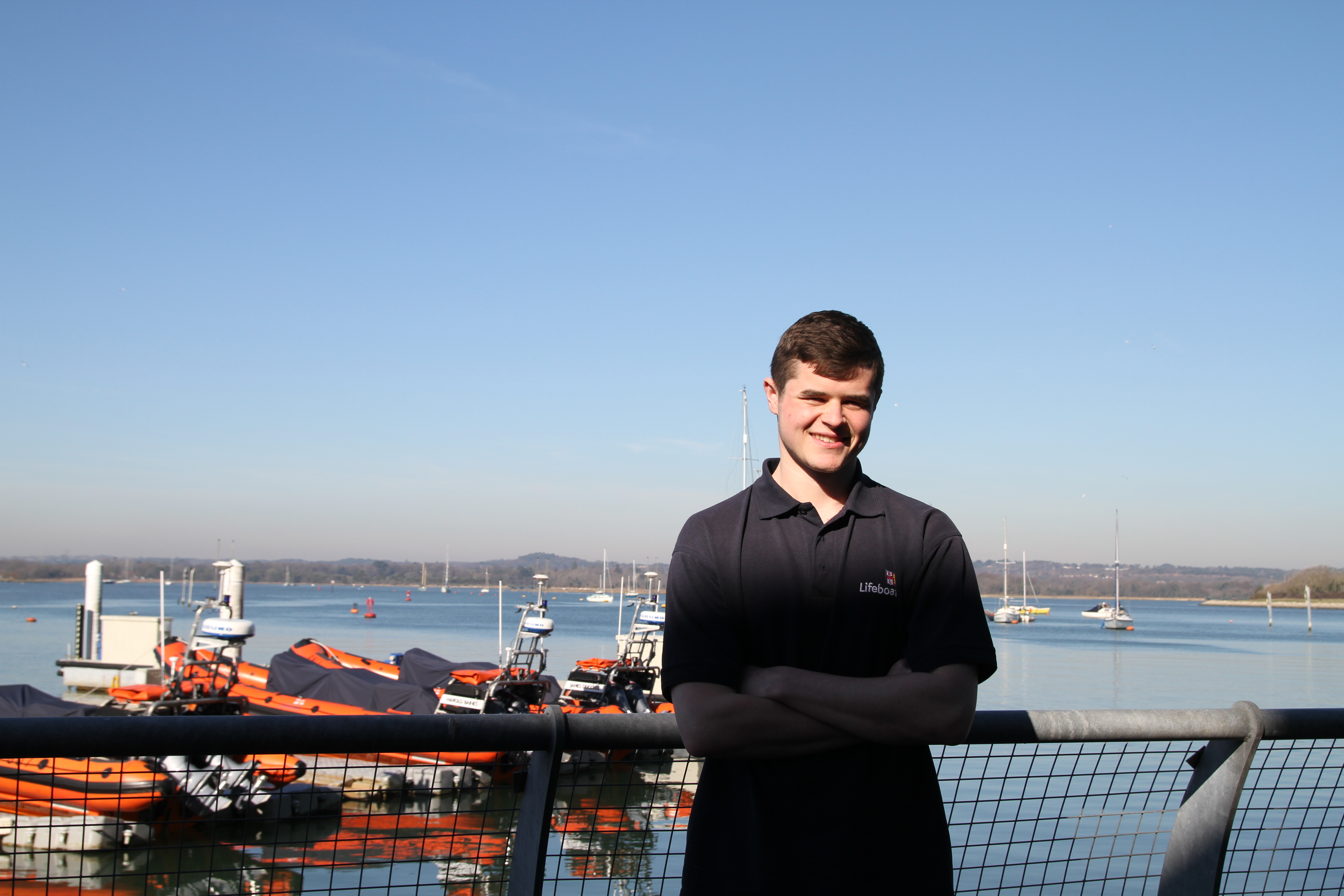 RNLI apprentice Boatbuilder Eoin O'Connor standing in front of inshore lifeboats on the water