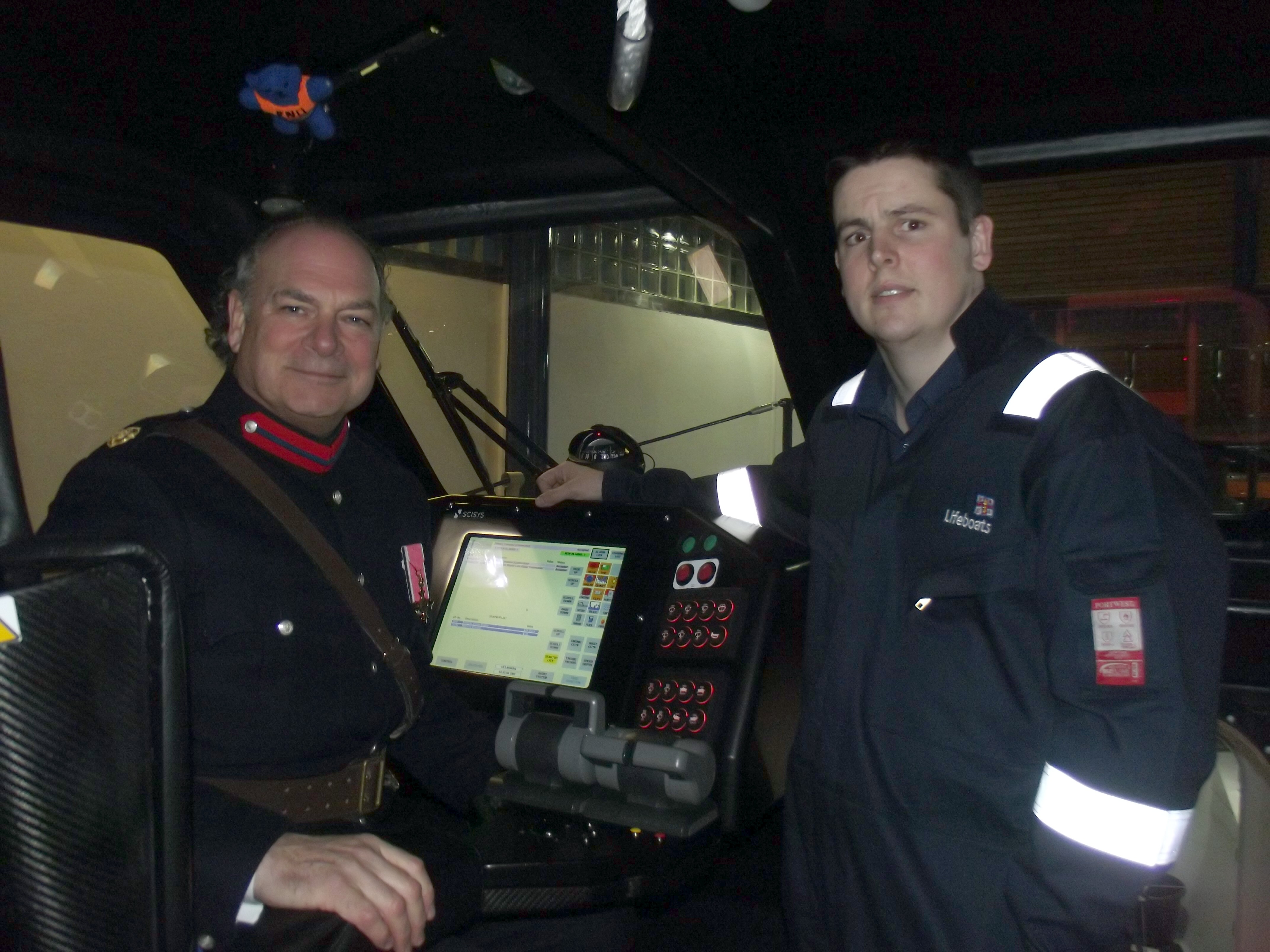 Two men, one in uniform, inside a lifeboat with electronic equipment behind them