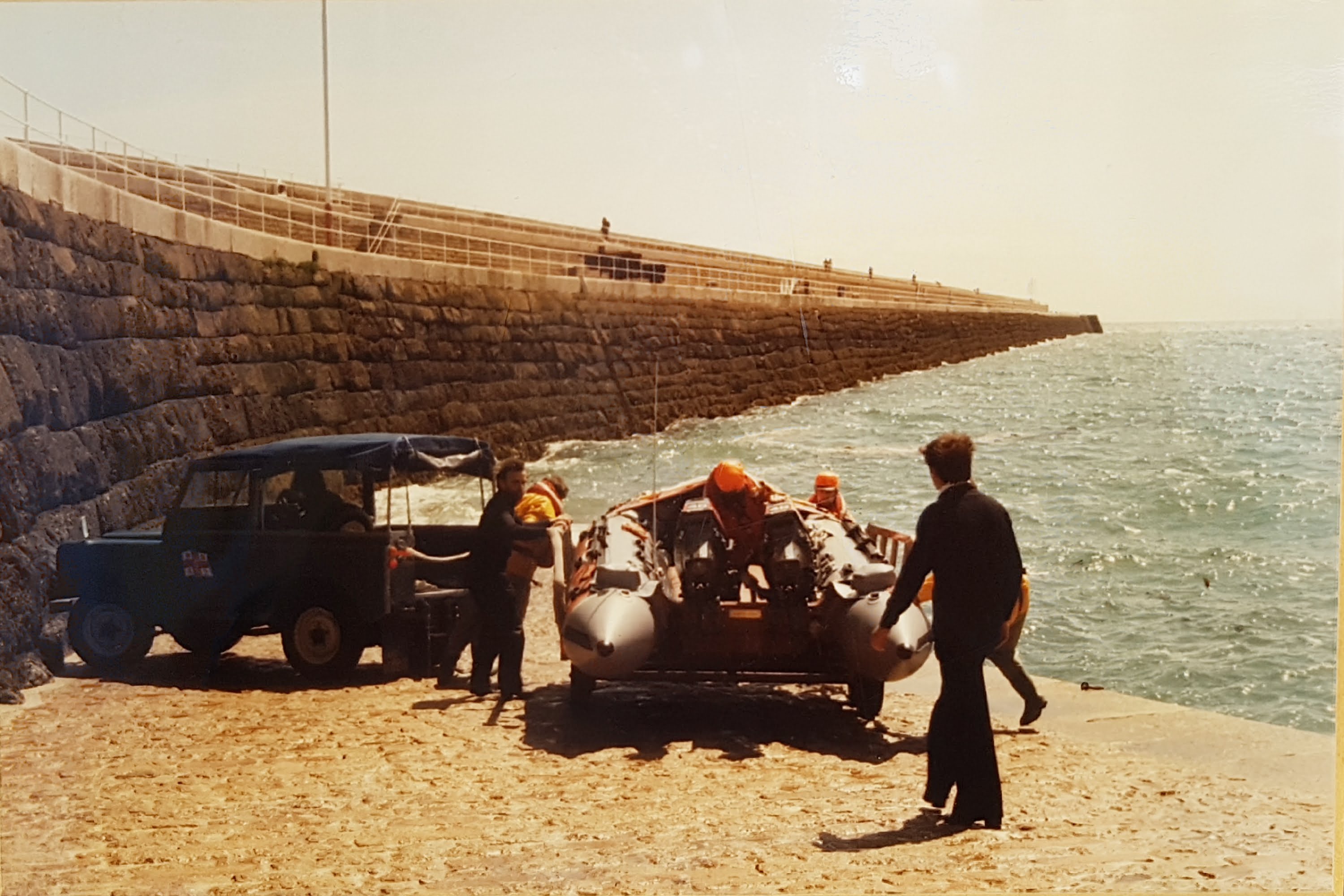 A faded colour photo showing the class-C lifeboat ready to be launched down the slip underneath St Catherine's breakwater on a hot sunny day. The breakwater itself extends into the distance.