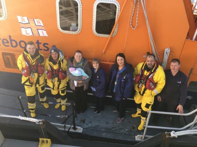 Lifeboat crew plus mum with baby and two midwives on side deck of lifeboat