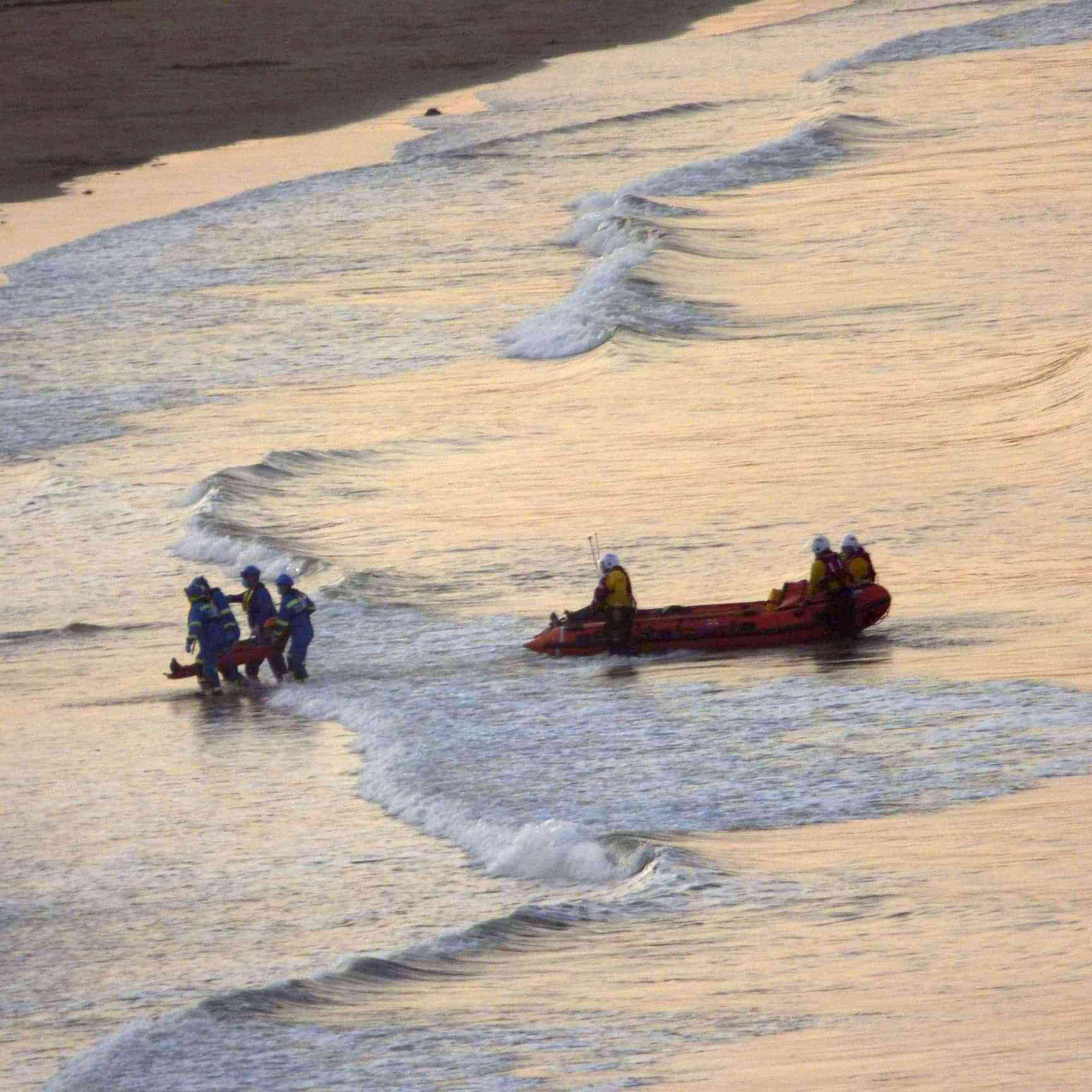 Lifeboat crew and coastguards carry the casualty to shore