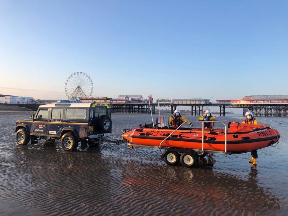 D class &amp; Landrover with volunteer crew on the beach with pier in the background