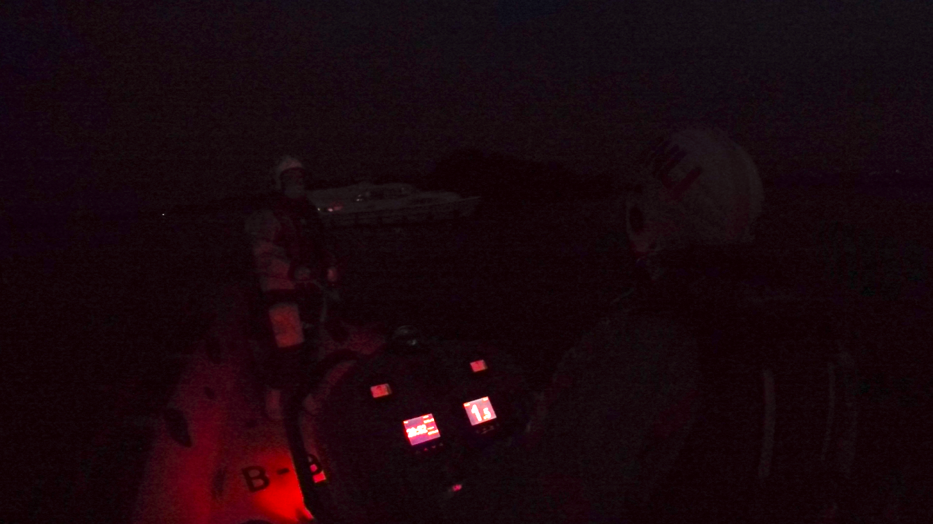 Lifeboat making a cautious approach to the casualty vessel, it's dark and the casualty vessel is a ghostly white over the bow of the lifeboat.