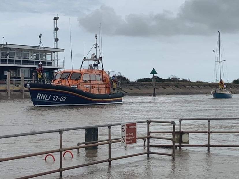 The lifeboat is towing a sailing boat down a river