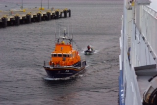 The lifeboat is towing the RIB past the Hamnavoe car ferry seen moored on the right