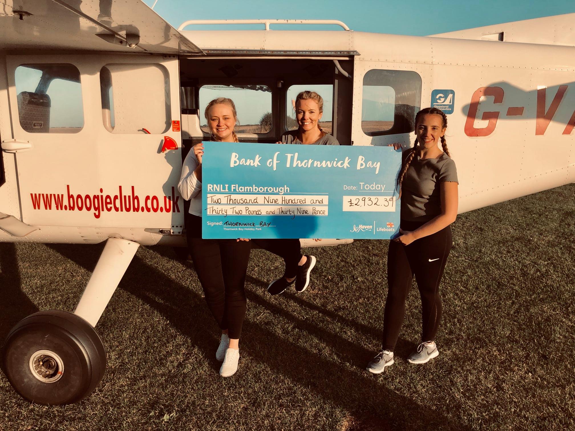 Three team members from Haven's Thornwick Bay holiday sitting on a light aircraft holding a cheque for a sponsored skydive