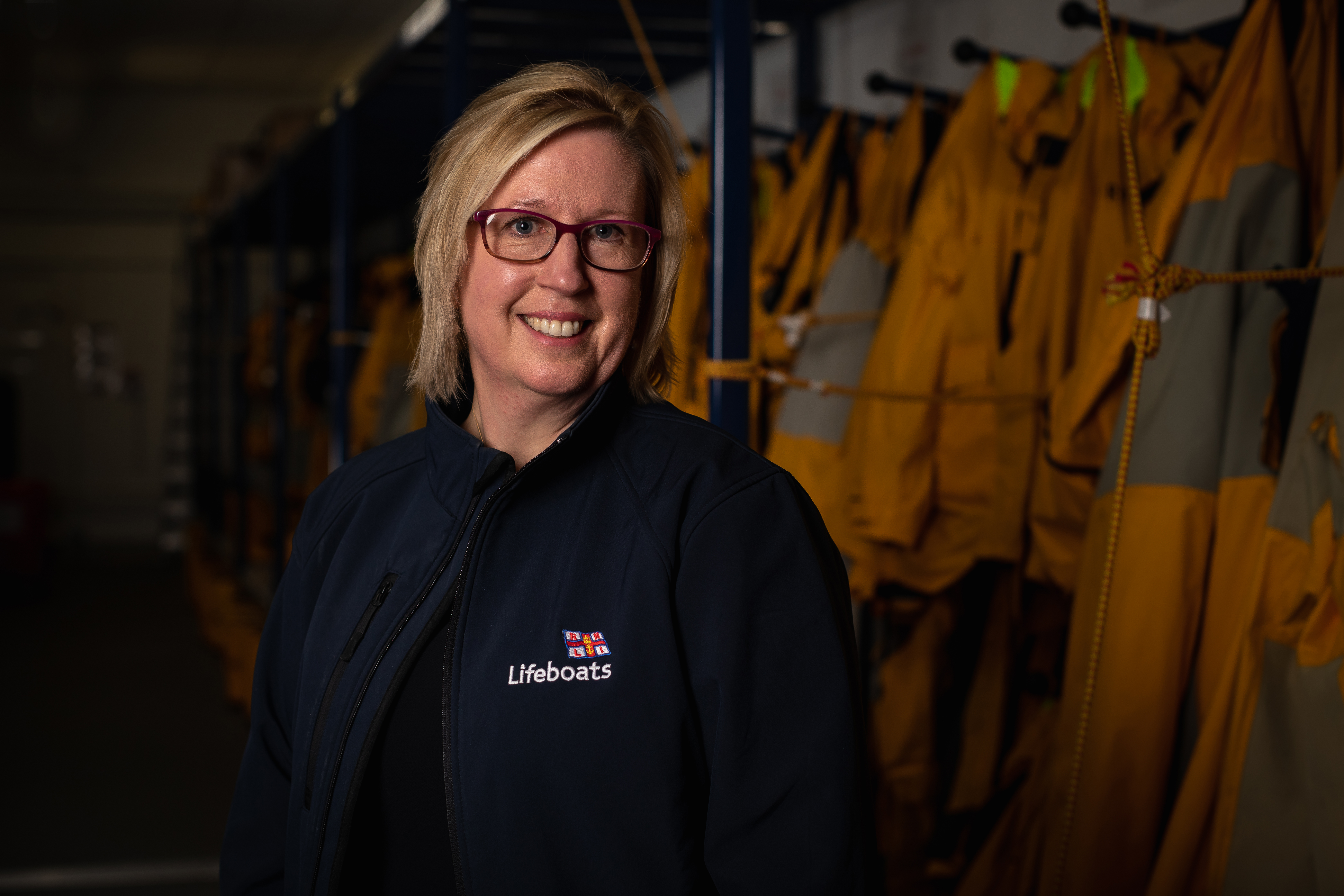 Sue Barnes stood in front of lifeboat crew kit hanging up behind her