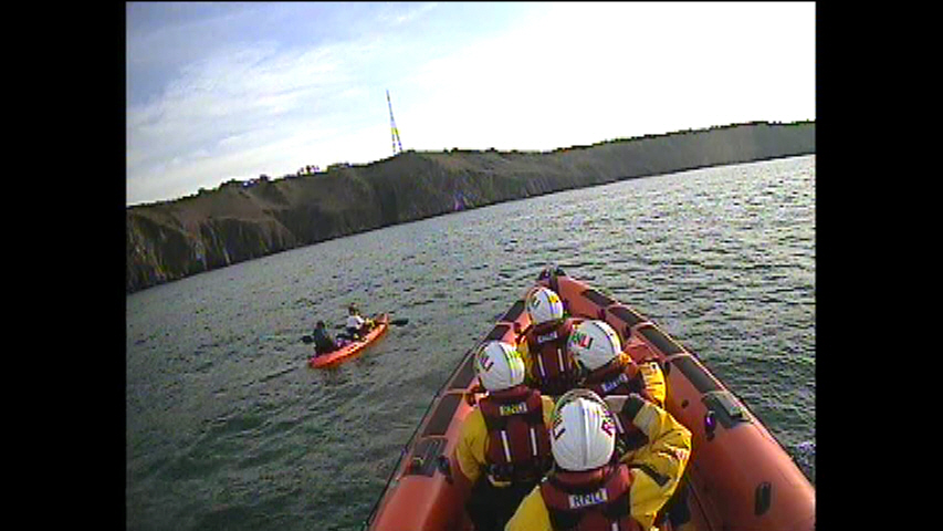 The Atlantic 85 inshore lifeboat approaches the double kayak in calm conditions with the north coast of Jersey in the background