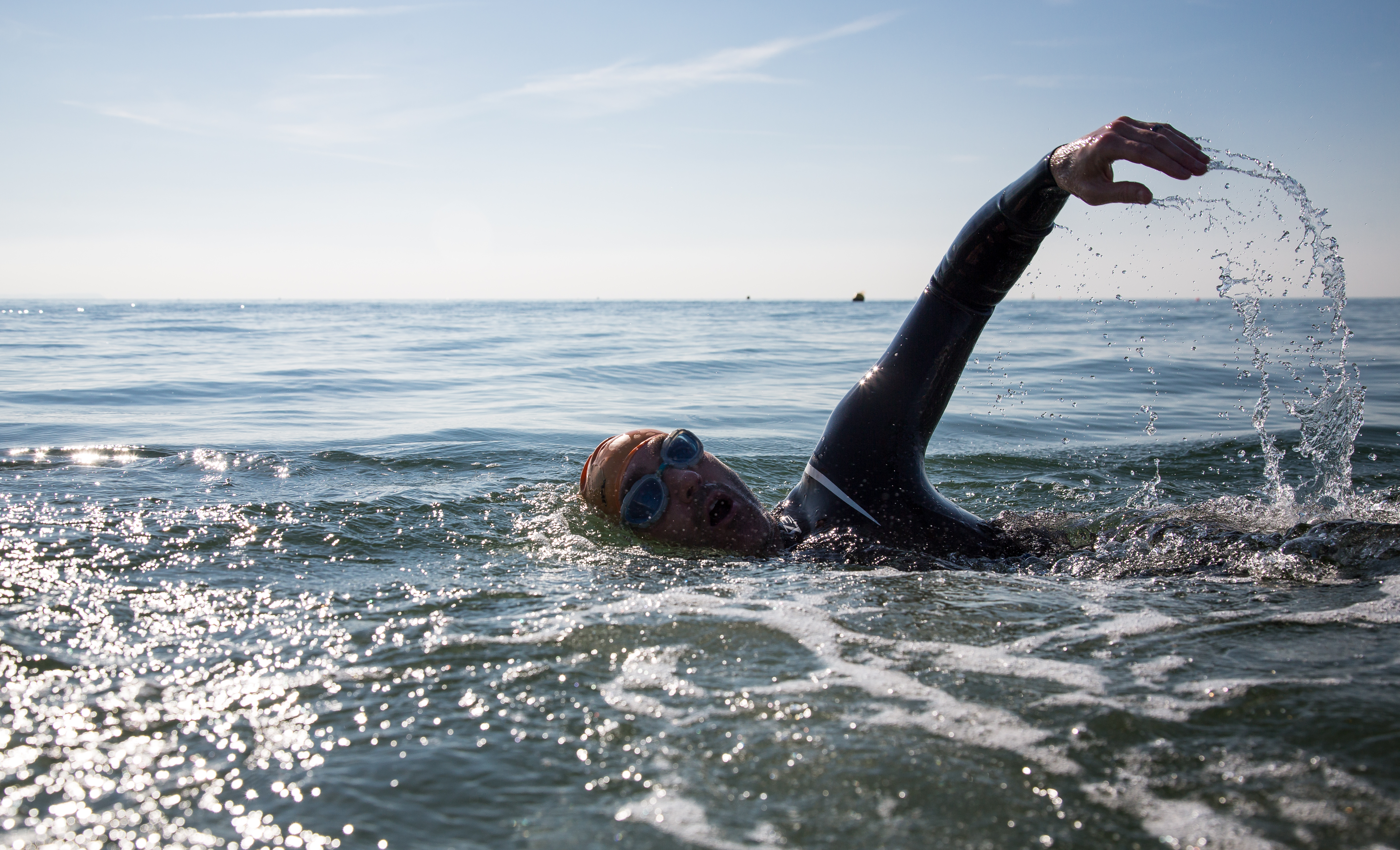 A man swimming in the sea in a wetsuit and bright swimming cap 