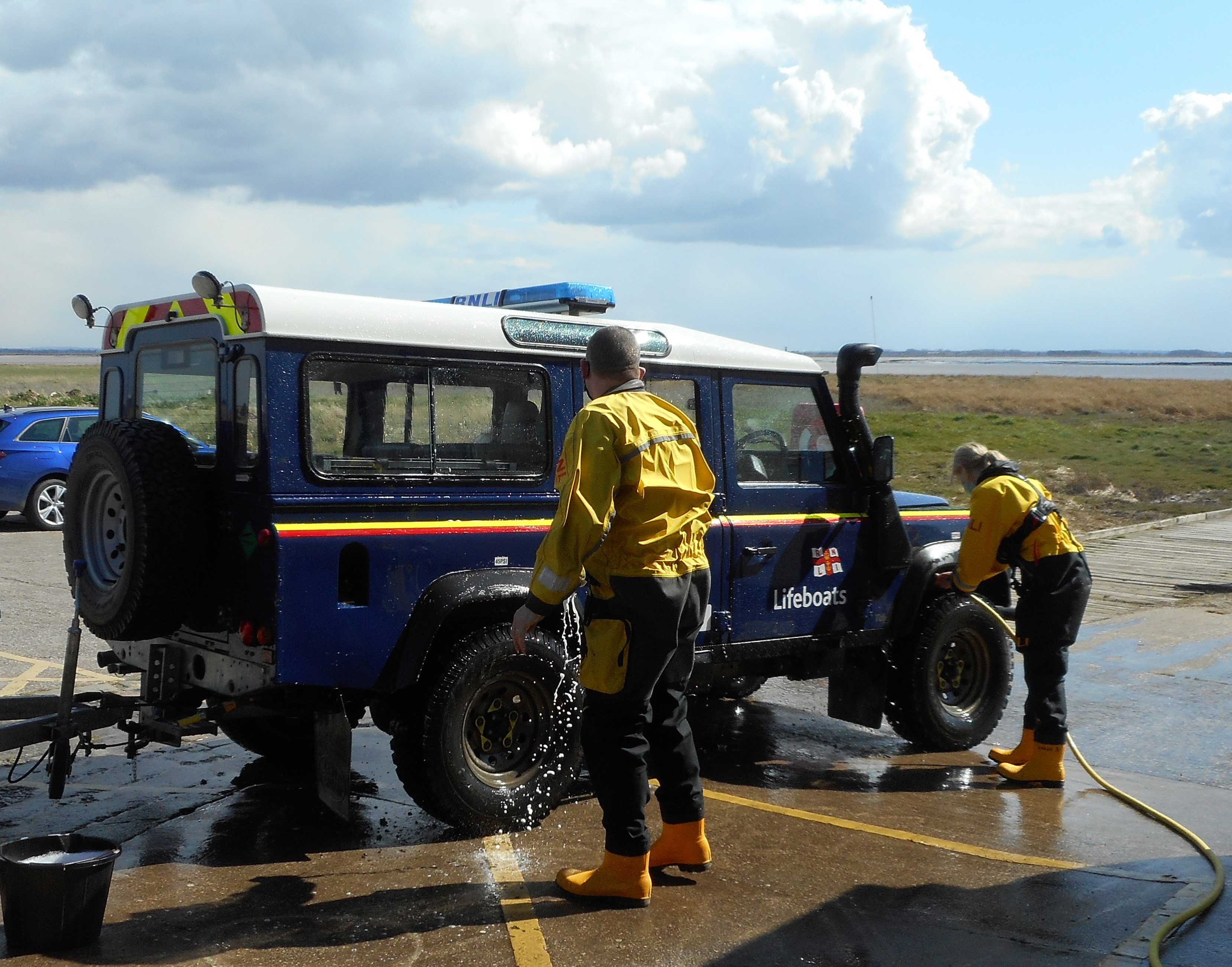 A Land Rover is being cleaned by two crew in wet suites.