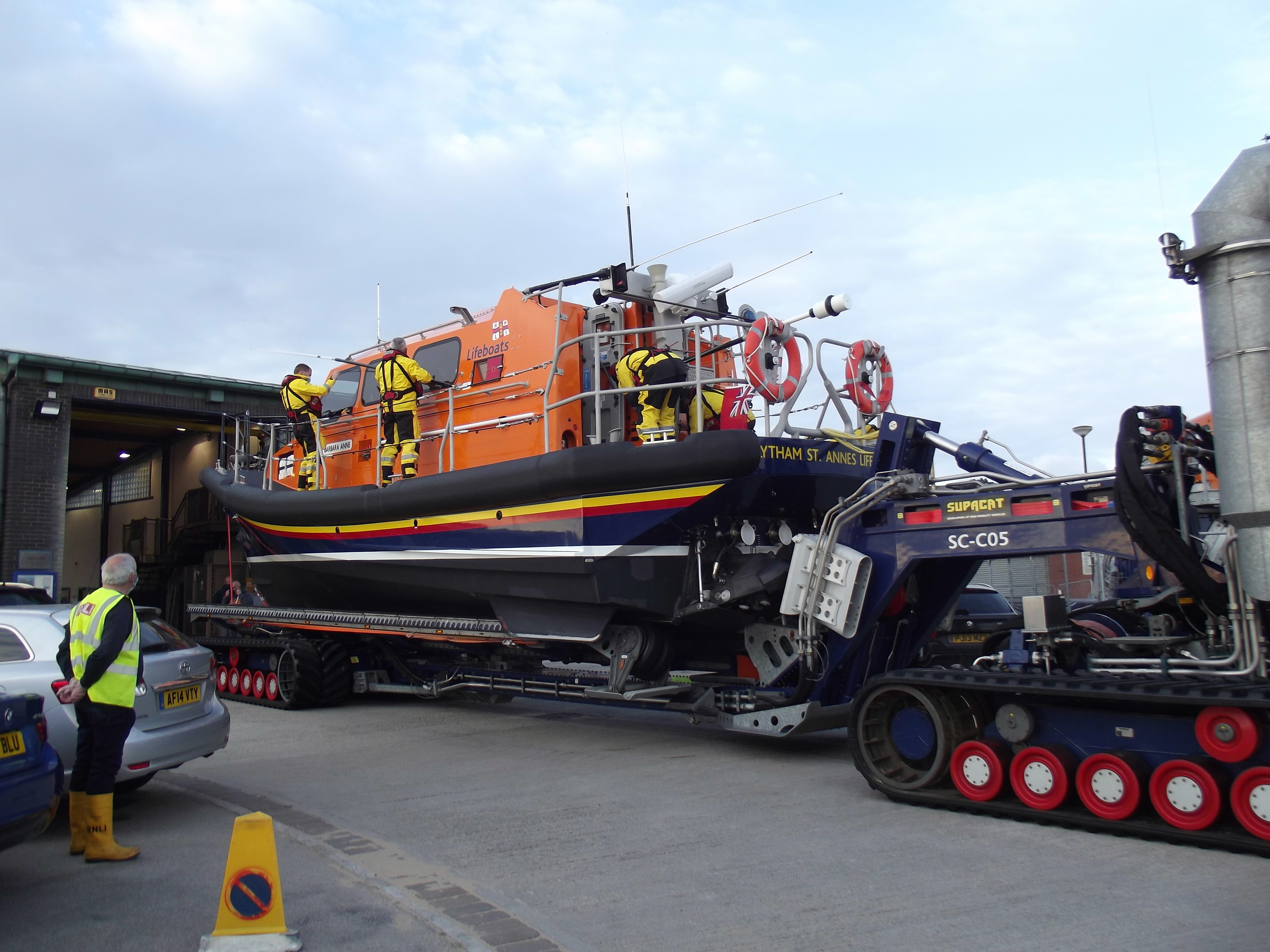 A lifeboat sits on her launching carriage while crew busy themselves to raise aerials etc
